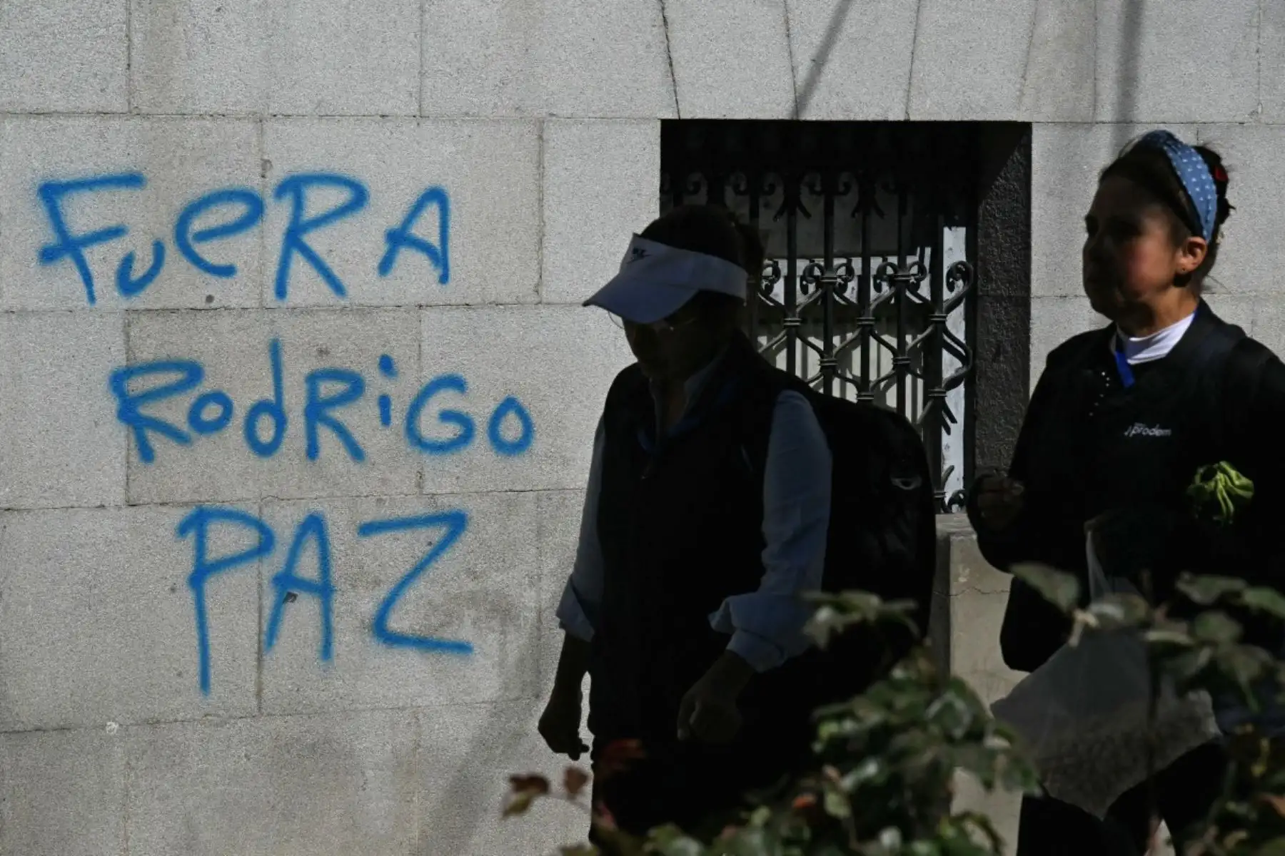 Mujeres pasan por un grafiti que lee "Rodrigo Paz fuera", refiriéndose al presidente de Bolivia en La Paz, el 19 de mayo de 2026, el día después de una protesta exigiendo su renuncia. Foto: AFP