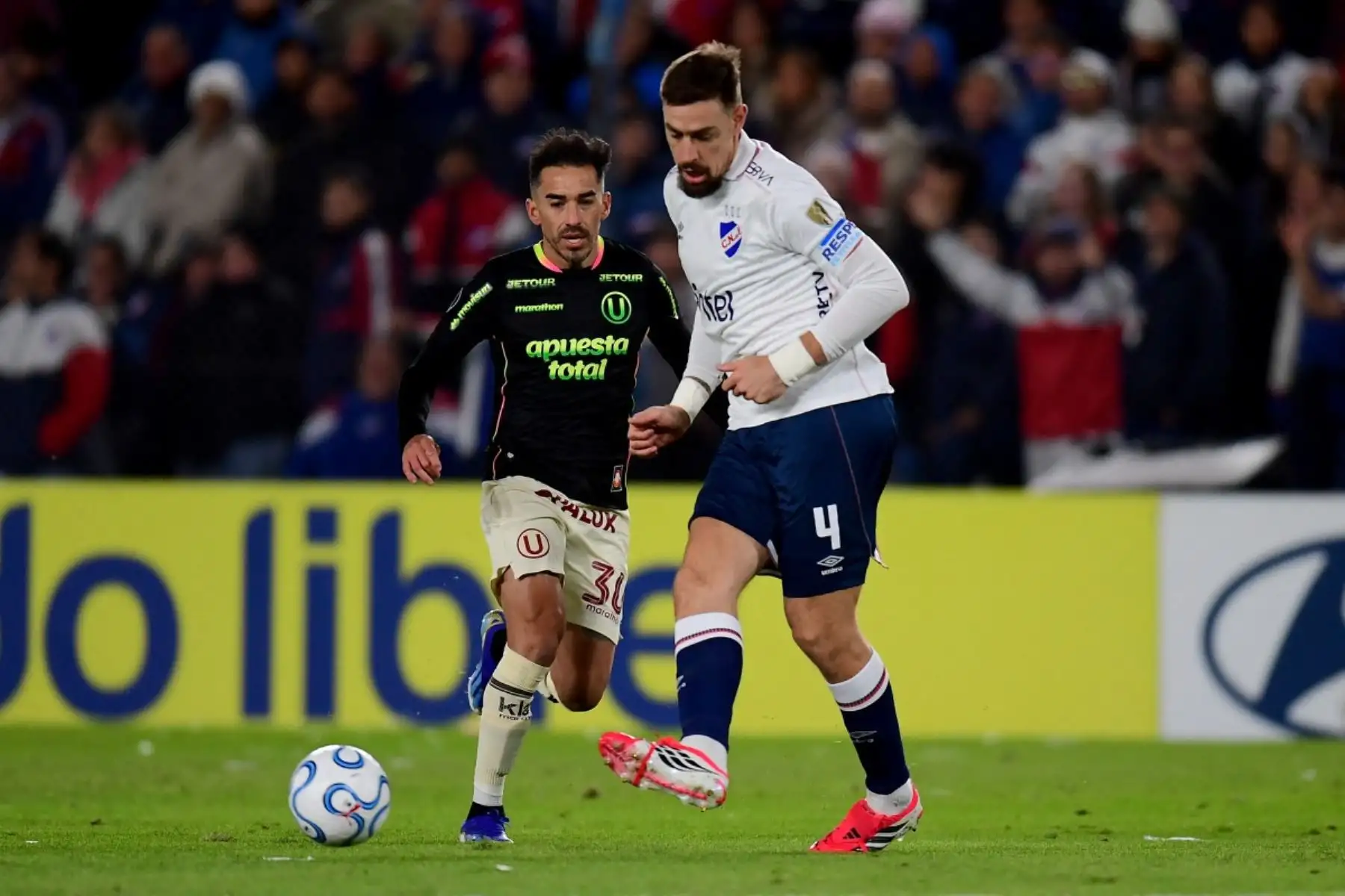 El defensor de Nacional  Sebastián Coates pasa el balón por delante del delantero de Universitario  Lisandro Alzugaray durante el partido de fútbol de la fase de grupos de la Copa Libertadores entre Nacional de Uruguay y Universitario de Perú. Foto: AFP