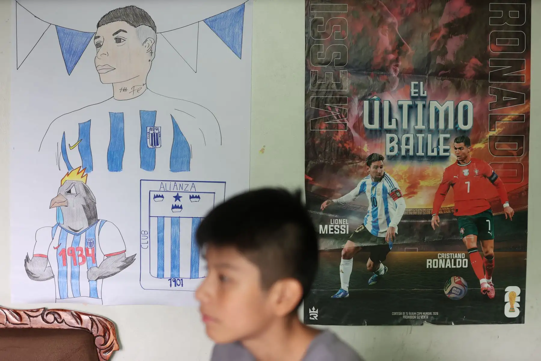 Mathías observa uno de los pósteres de fútbol que decoran su habitación, espacio donde desarrolla gran parte de los dibujos y figuras de su álbum mundialista artesanal. Foto: ANDINA/Melina Mejía.