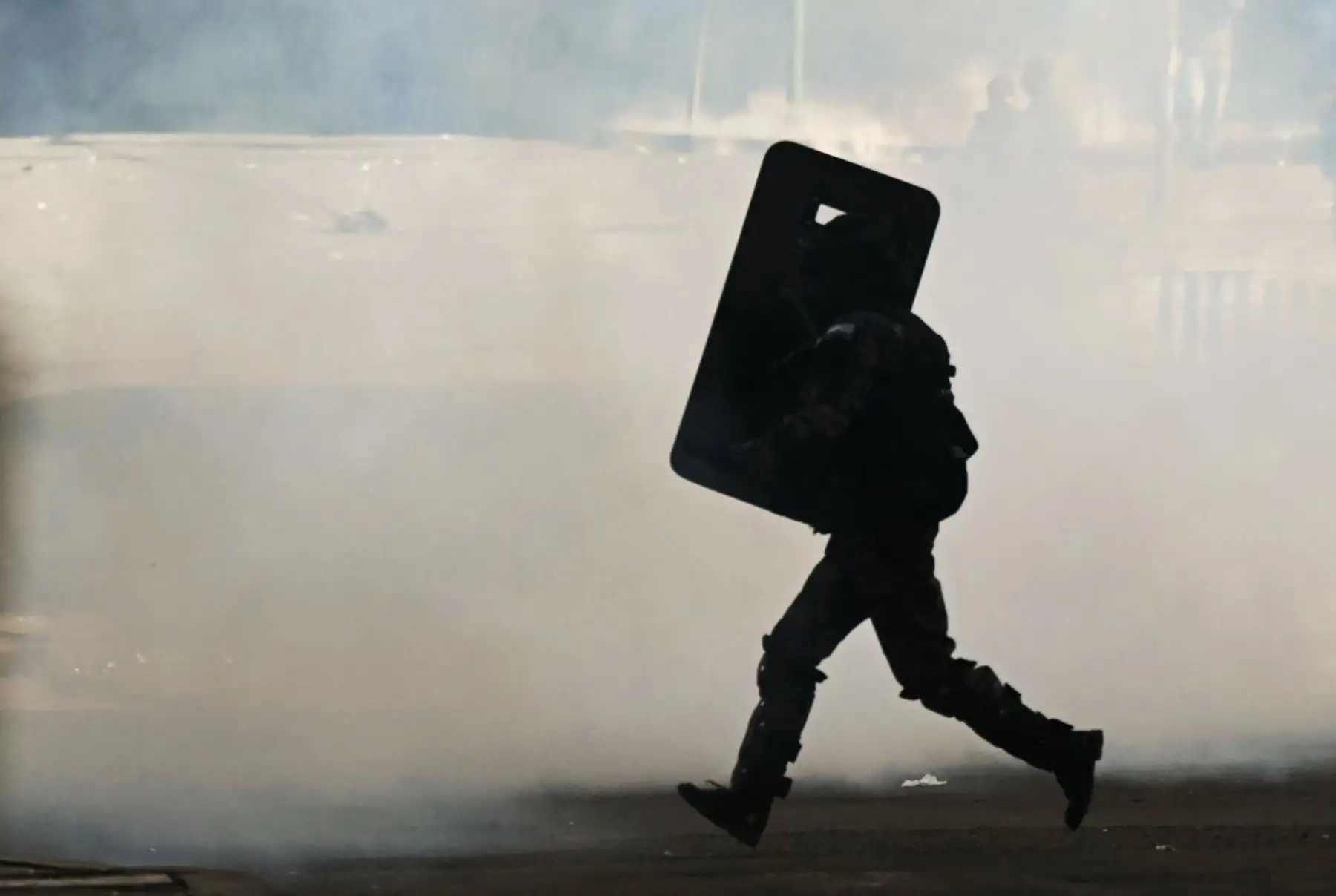 Un policía antimotines corre entre una nube de gas lacrimógeno durante los disturbios registrados en el centro de La Paz, donde las fuerzas del orden dispersaron a manifestantes que intentaban acercarse a la sede del gobierno boliviano. Foto: AFP.