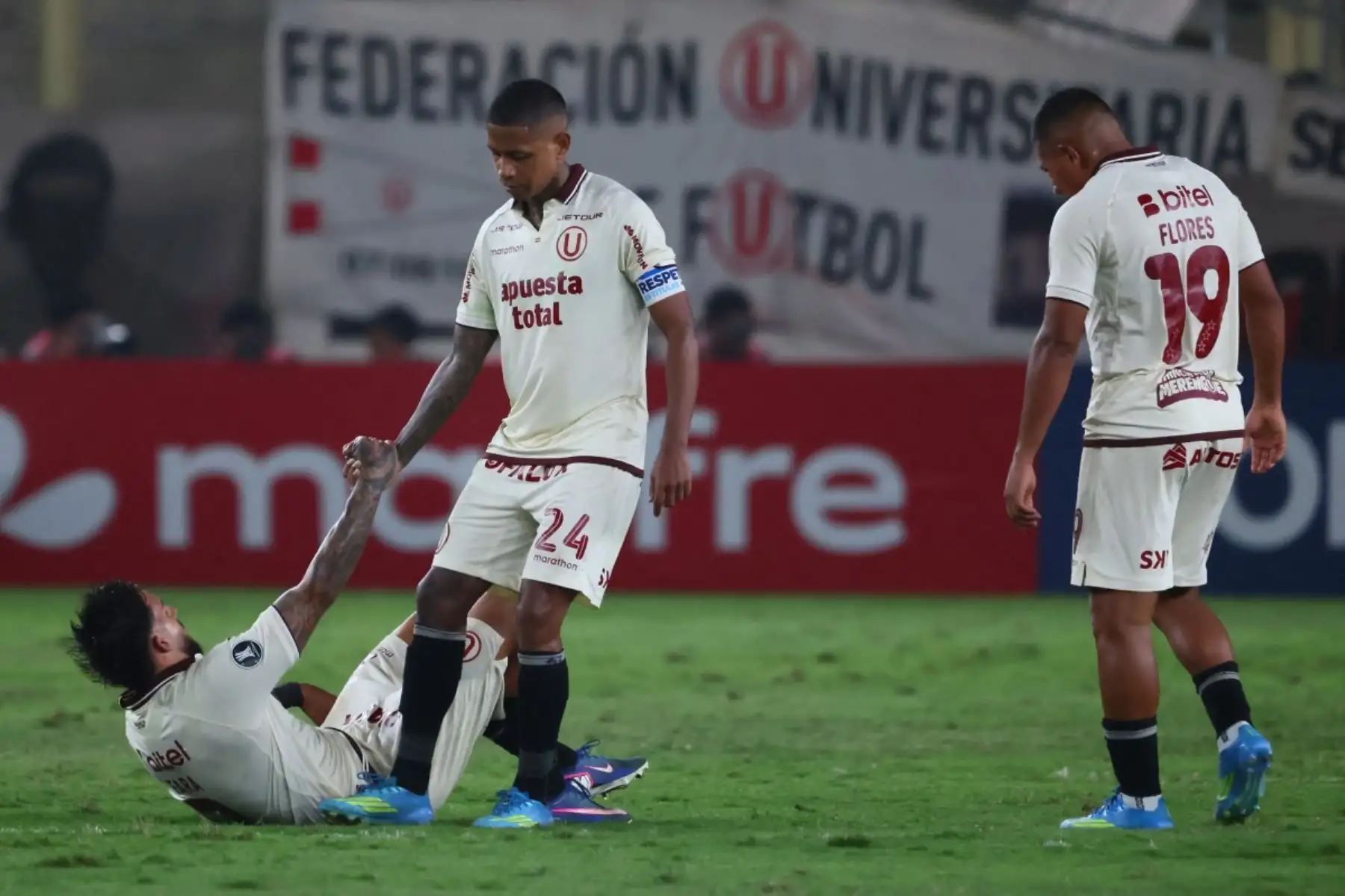 El delantero número 24 del Universitario, Andy Polo, ayuda a su compañero, el defensa argentino número 02, Cain Fara, a levantarse junto al delantero número 19, Edison Flores, al final del partido de la fase de grupos de la Copa Libertadores entre el Universitario de Perú y el Deportes Tolima de Colombia, disputado en el Estadio Monumental "U" Marathon de Lima el 26 de mayo de 2026. (Foto de Connie FRANCE / AFP)