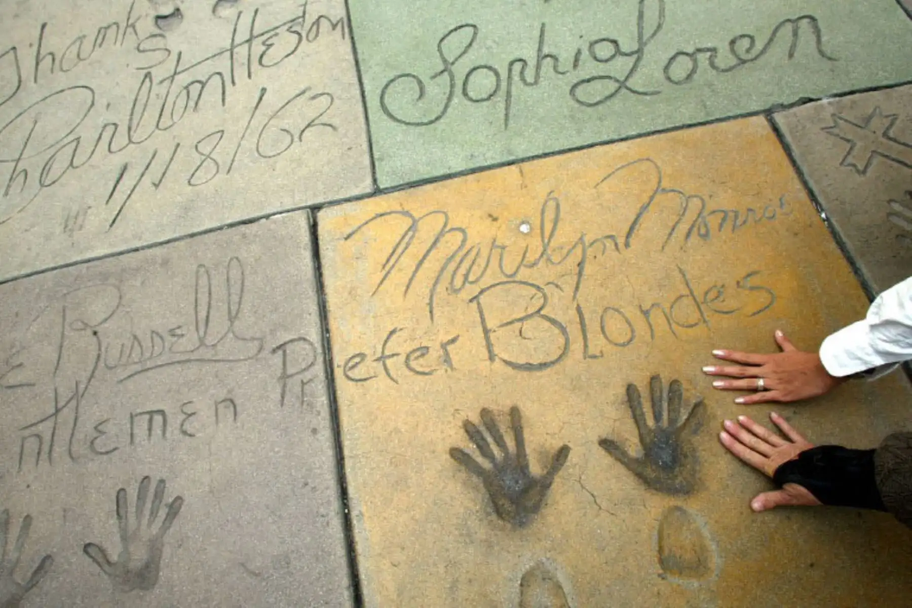 Turistas colocan sus manos sobre una placa de cemento que representa las manos y los zapatos de Marilyn Monroe en el Teatro Chino de Hollywood, el 24 de octubre de 2002. Foto: AFP