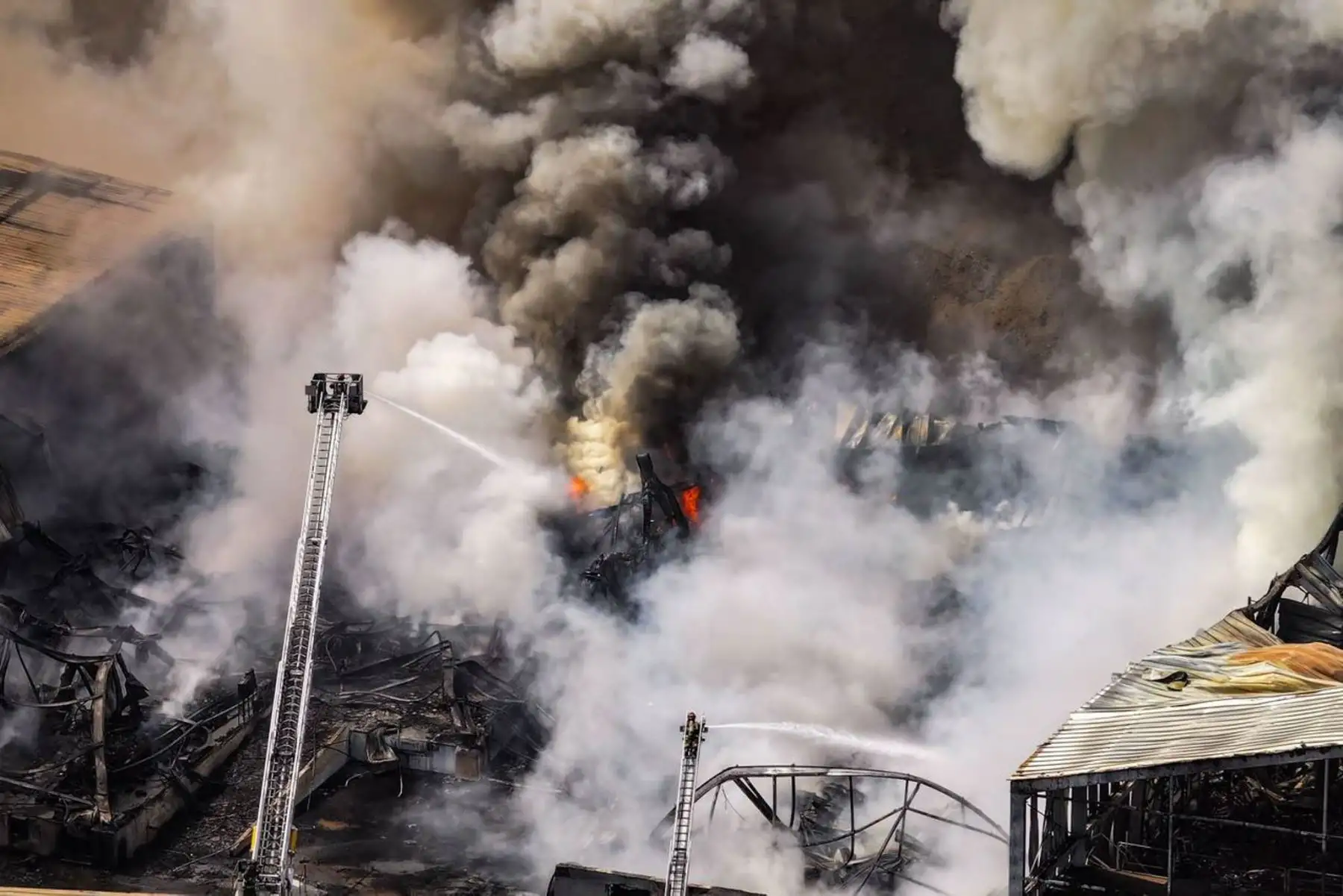 Densas columnas de humo se elevan sobre la zona industrial de Lurín mientras los bomberos continúan trabajando para controlar los focos activos del incendio. Foto: Ricardo Cuba.