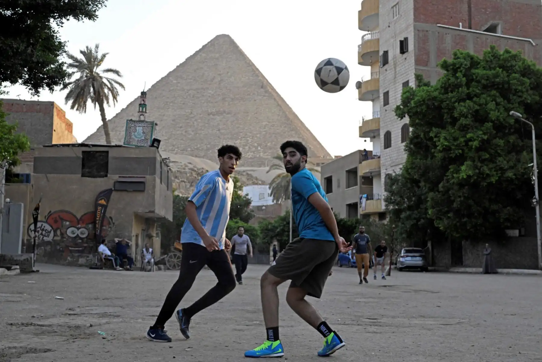 Jugadores egipcios juegan al fútbol en una calle del barrio de Nazlet el-Semman, junto a las Grandes Pirámides de Giza en El Cairo. Egipto debuta en la Copa Mundial de la FIFA 2026 contra Bélgica en Seattle el 15 de junio, antes de enfrentarse a Nueva Zelanda e Irán en el Grupo G. Foto: AFP