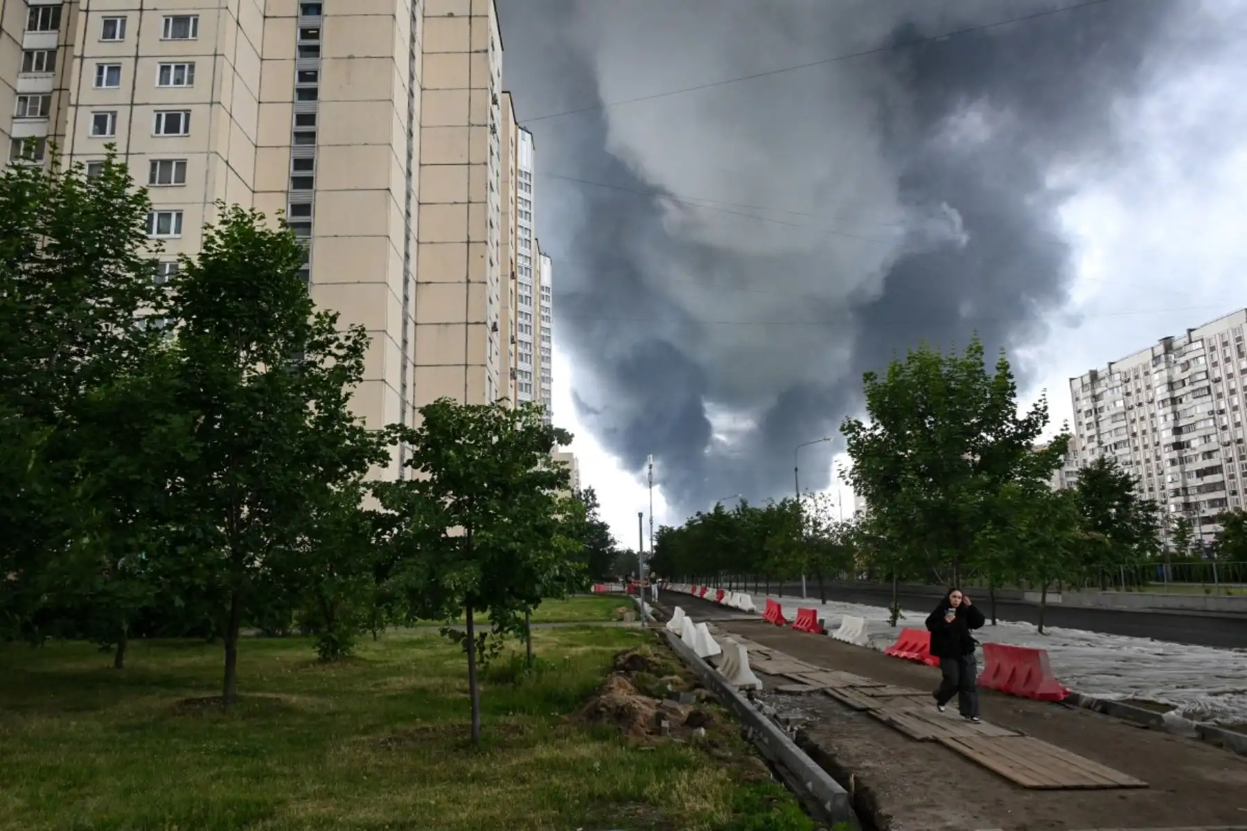 Una mujer camina por una zona residencial mientras una columna de humo negro se eleva desde la refinería de petróleo de la petrolera rusa Gazprom Neft en las afueras del sureste de Moscú. Foto: AFP