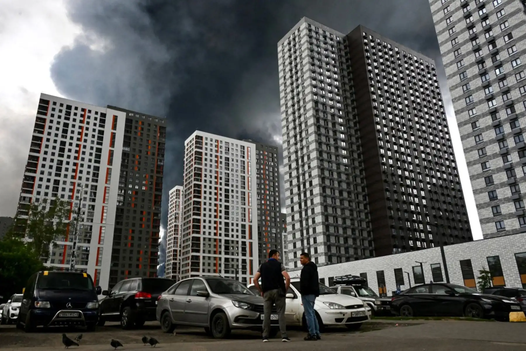 Personas caminan por una zona residencial mientras una columna de humo negro se eleva desde la refinería de petróleo de la petrolera rusa Gazprom Neft en las afueras del sureste de Moscú. Foto: AFP