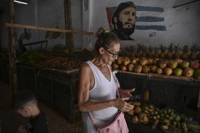 Una mujer revisa su celular en un mercado de agricultores en La Habana el 18 de junio de 2026, junto a una imagen de Fidel Castro. Foto: AFP