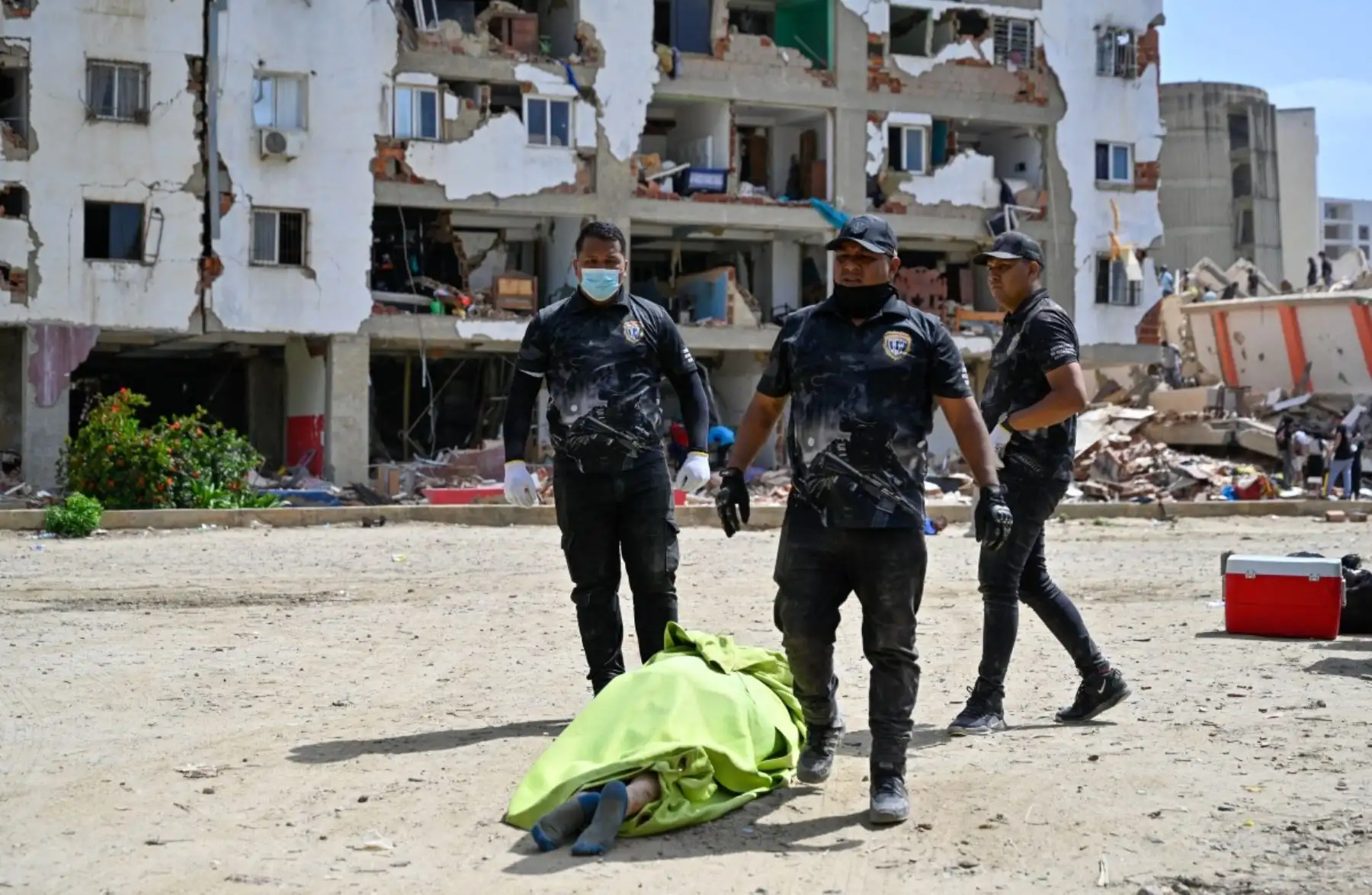 Miembros de la policía forense venezolana se encuentran junto a un cuerpo cubierto con una sábana verde en el lugar donde se derrumbaron edificios tras los terremotos en Caraballeda, estado de La Guaira, Venezuela, el 26 de junio de 2026. Foto: AFP