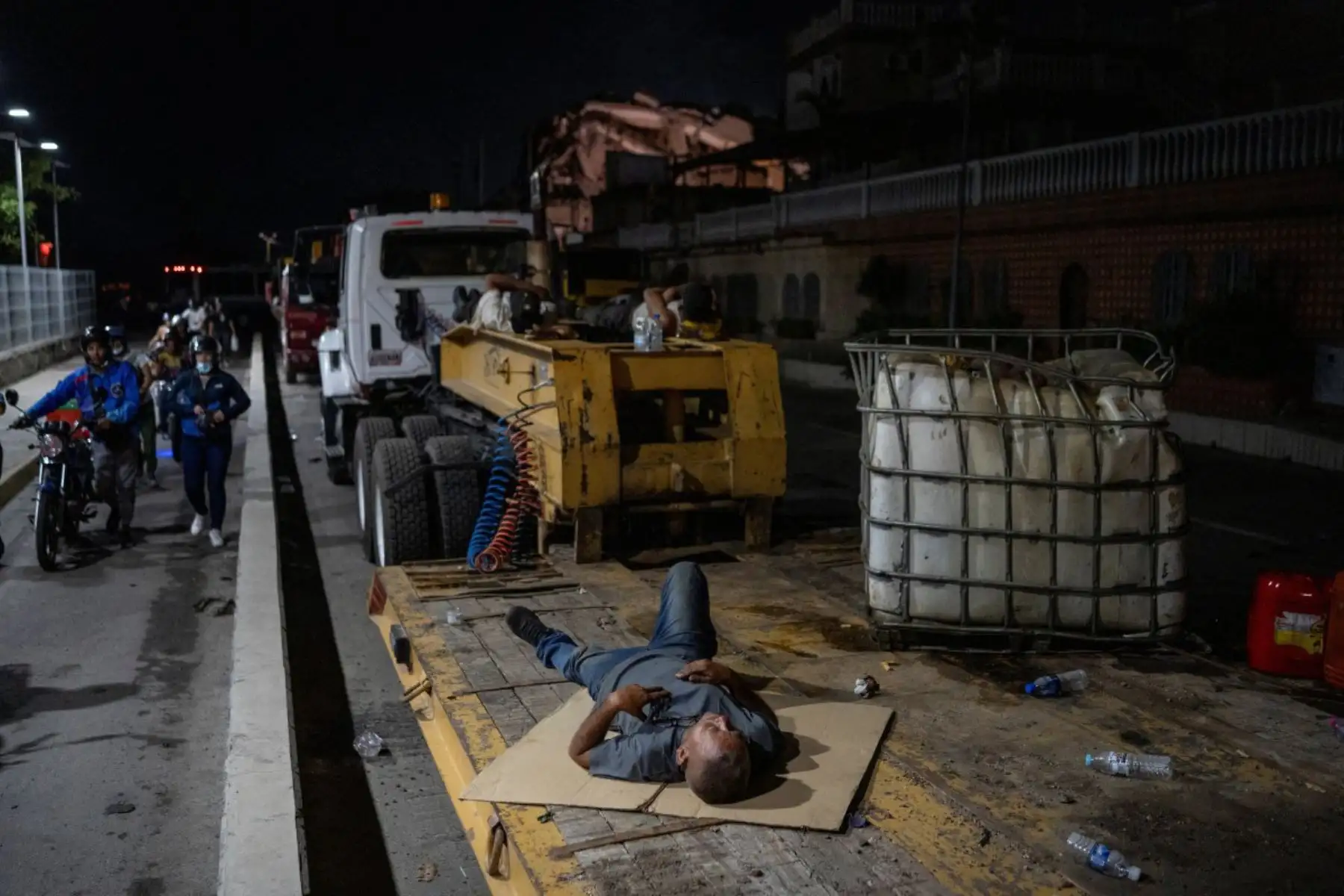 Un hombre duerme en la parte trasera de un camión cerca de un edificio derrumbado en La Guaira. El número de muertos por los dos fuertes terremotos que devastaron Venezuela a principios de esta semana ascendió a 920 el 26 de junio, según informó el presidente de la Asamblea Nacional, Jorge Rodríguez. Foto: ANDINA/AFP