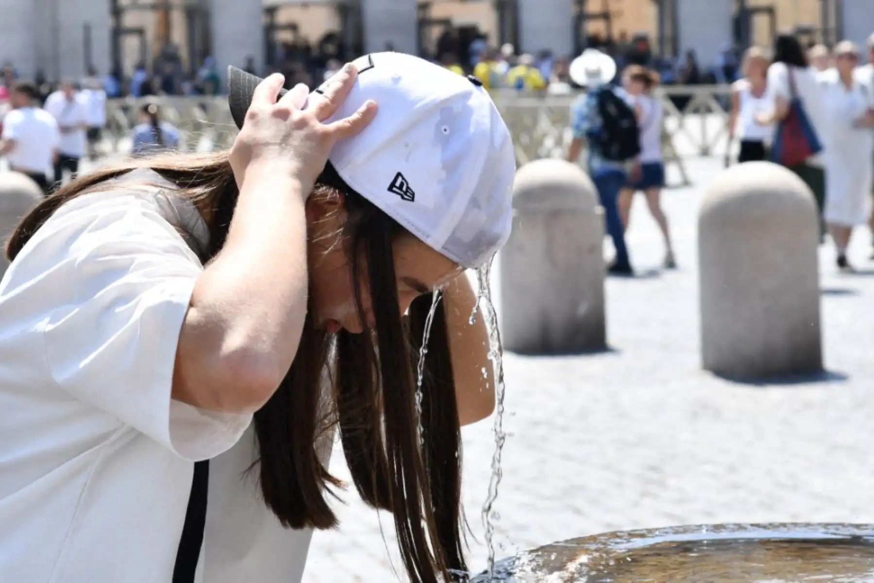 Una mujer se refresca en una fuente mientras espera el rezo del Ángelus dominical, oficiado por el Papa León XIV en la Plaza de San Pedro, en el Vaticano. Foto: ANDINA/AFP