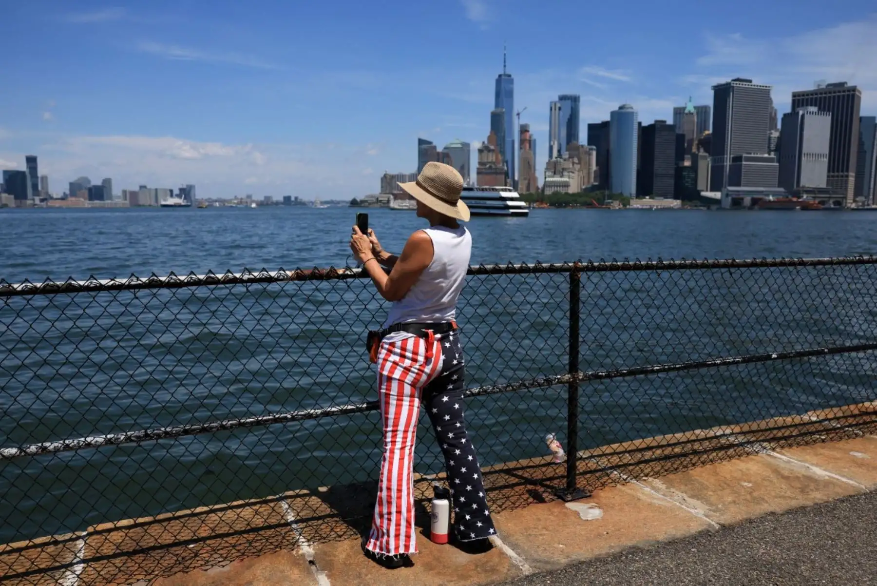 Una persona con pantalones con la bandera estadounidense toma fotografías del puerto de Nueva York el 4 de julio de 2026. Millones de estadounidenses celebraron el sábado el 250 aniversario del país. Foto: AFP