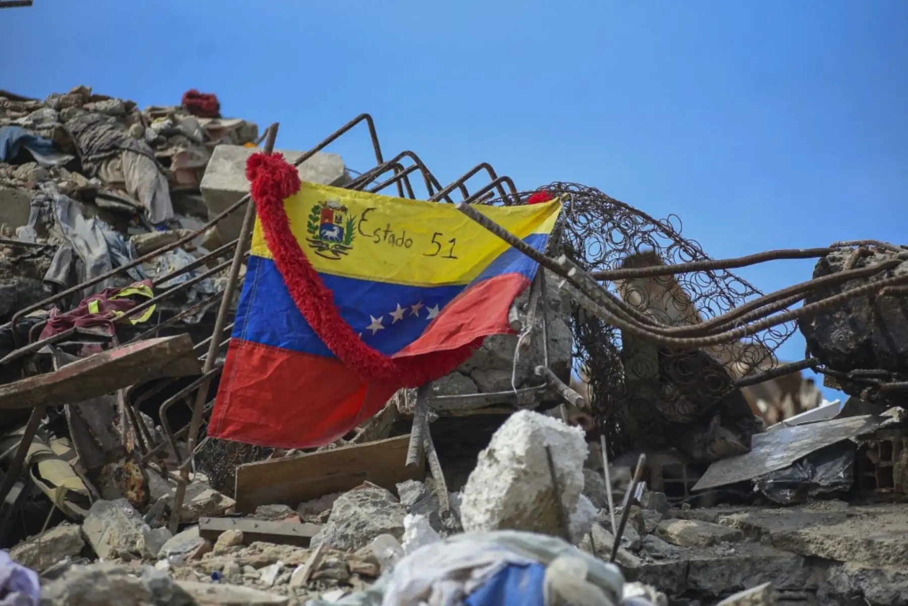 Una bandera nacional venezolana con la frase en español "Estados 51" cuelga entre los escombros de edificios destruidos por terremotos en La Guaira, Venezuela. Foto: AFP