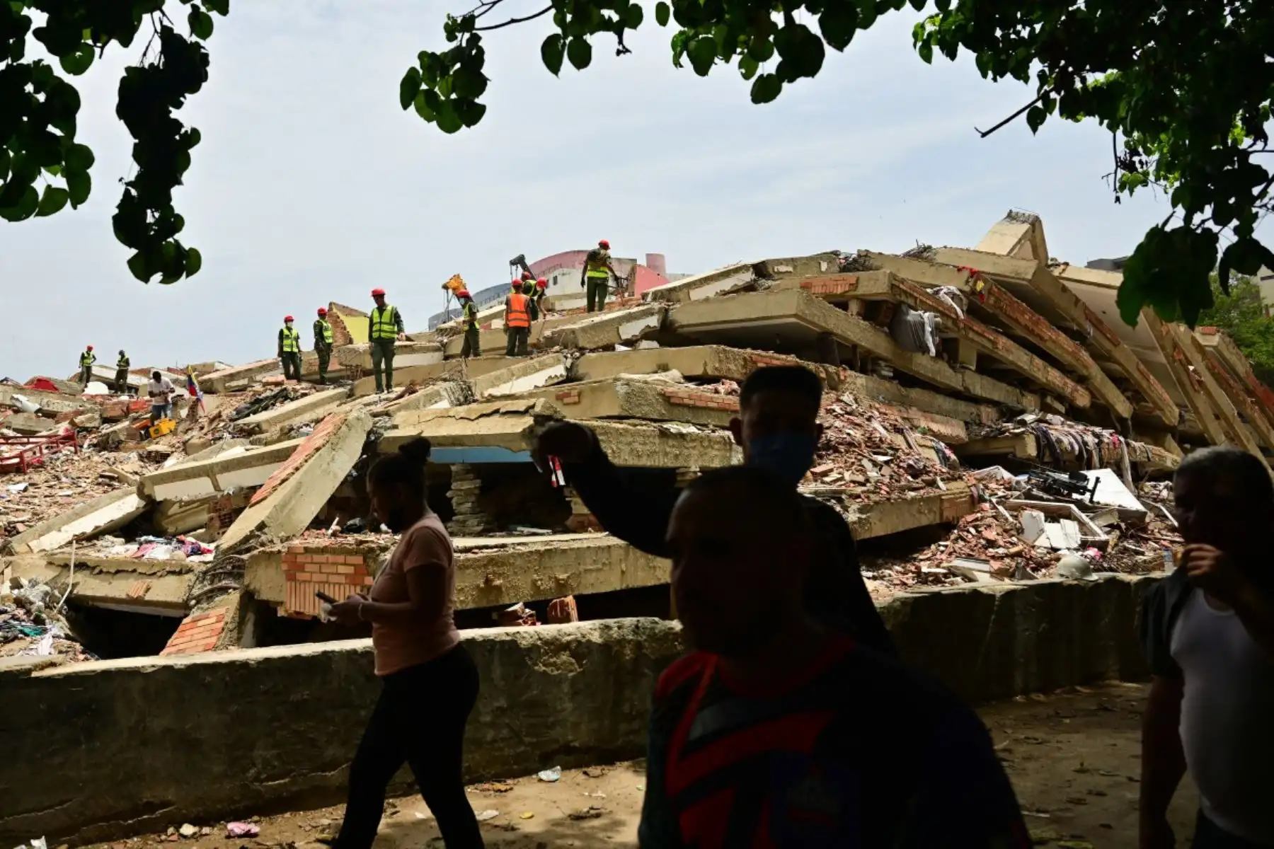 Personas pasan junto a un edificio derrumbado mientras personal militar lleva a cabo labores de retirada de escombros en Caraballeda, estado de La Guaira (Venezuela), el 12 de julio de 2026, tras los dos terremotos que azotaron la región.
La cifra de fallecidos por los dos terremotos que sacudieron Venezuela el 24 de junio ha superado los 4.300, según informó el 11 de julio el presidente de la Asamblea Nacional, Jorge Rodríguez. Foto: AFP