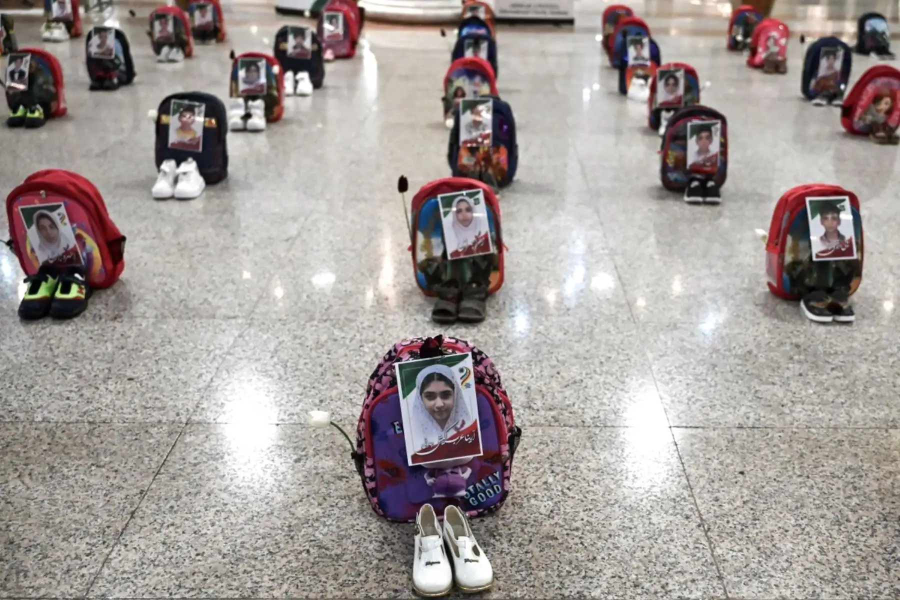 Retratos de escolares fallecidos en un ataque aéreo en Minab en febrero de 2026 fueron pegados en mochilas exhibidas junto a zapatos en el Aeropuerto Internacional Hashemi Nejad en Mashhad el 8 de julio de 2026, antes de la etapa final del funeral del líder asesinado Ali Khamenei. Fotos: AFP