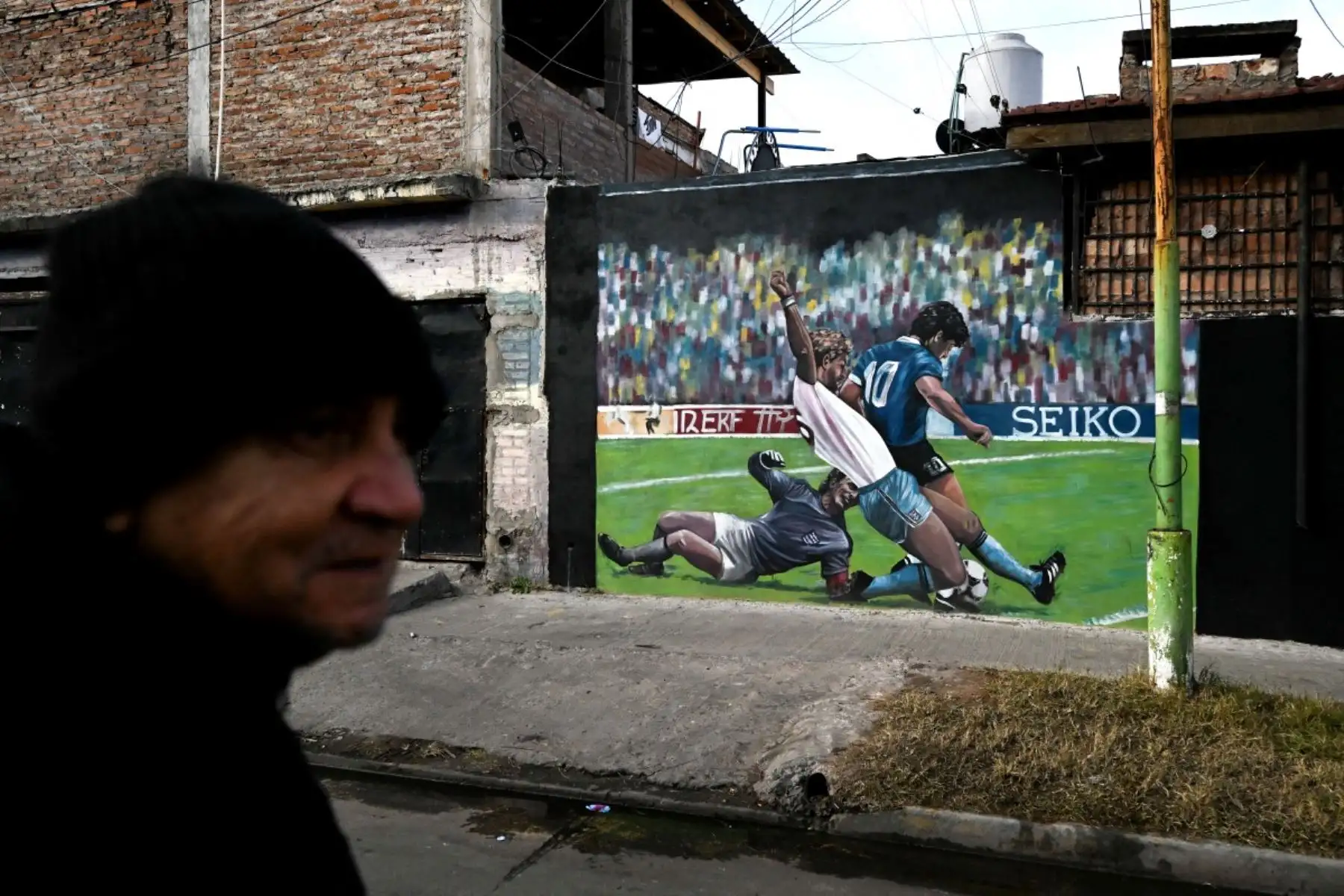Un hombre pasa junto a un mural que representa al fallecido legendario futbolista argentino Diego Maradona durante el partido del Mundial de México 1986 contra Inglaterra, en Villa Fiorito, en las afueras de Buenos Aires, el 14 de julio de 2026. Foto: AFP