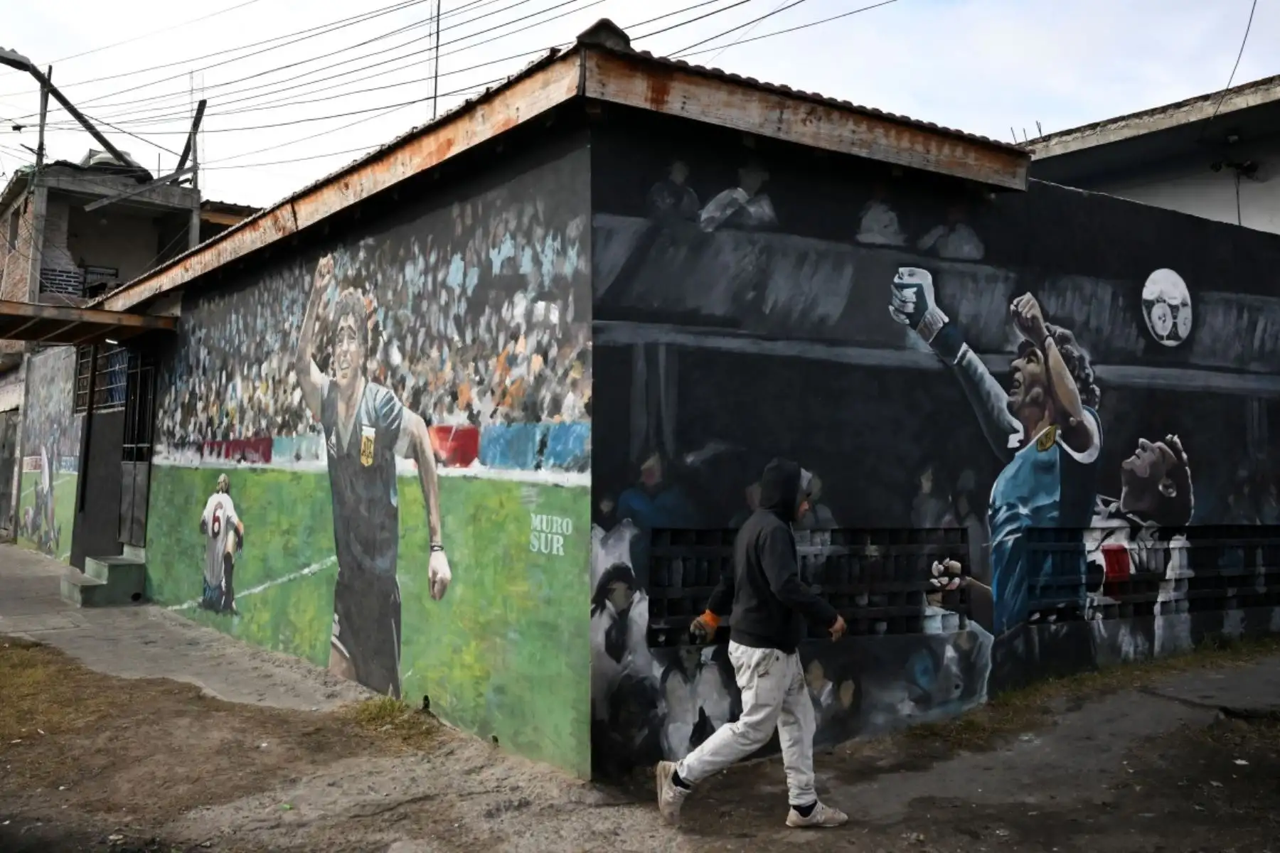 Un hombre pasa junto a un mural que representa al fallecido legendario futbolista argentino Diego Maradona durante el partido del Mundial de México 1986 contra Inglaterra, en Villa Fiorito, en las afueras de Buenos Aires, el 14 de julio de 2026. Foto: AFP