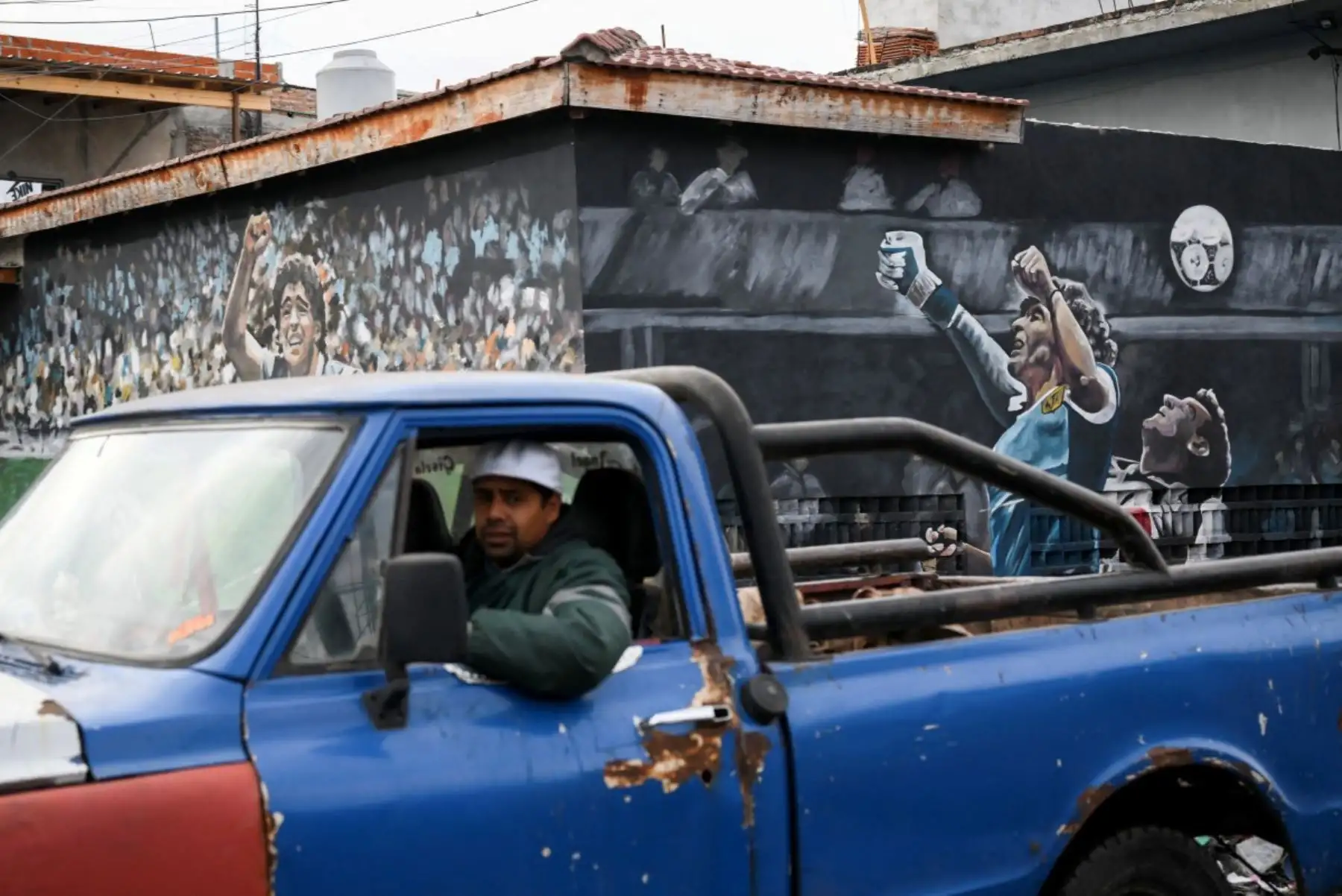 Un hombre conduce su camión junto a murales que representan al fallecido legendario futbolista argentino Diego Maradona durante el partido del Mundial de México 1986 contra Inglaterra, en Villa Fiorito, en las afueras de Buenos Aires, el 14 de julio de 2026. Foto: AFP