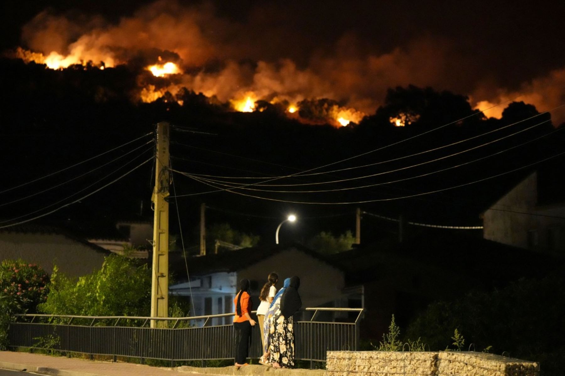 Los residentes observan las llamas en las cimas de las colinas mientras los bomberos combaten un incendio forestal en la zona de Cebreros, cerca de Ávila, a 80 km al oeste de Madrid, la noche del 24 de julio de 2026. Foto: AFP
