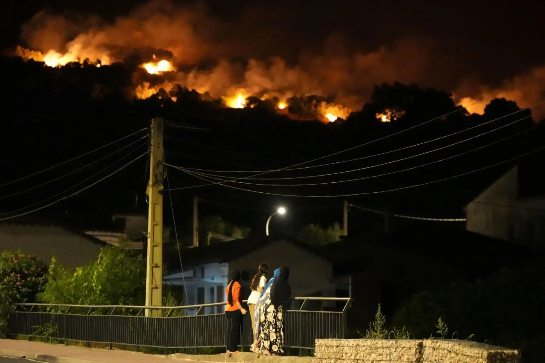 Los residentes observan las llamas en las cimas de las colinas mientras los bomberos combaten un incendio forestal en la zona de Cebreros, cerca de Ávila, a 80 km al oeste de Madrid, la noche del 24 de julio de 2026. Foto: AFP