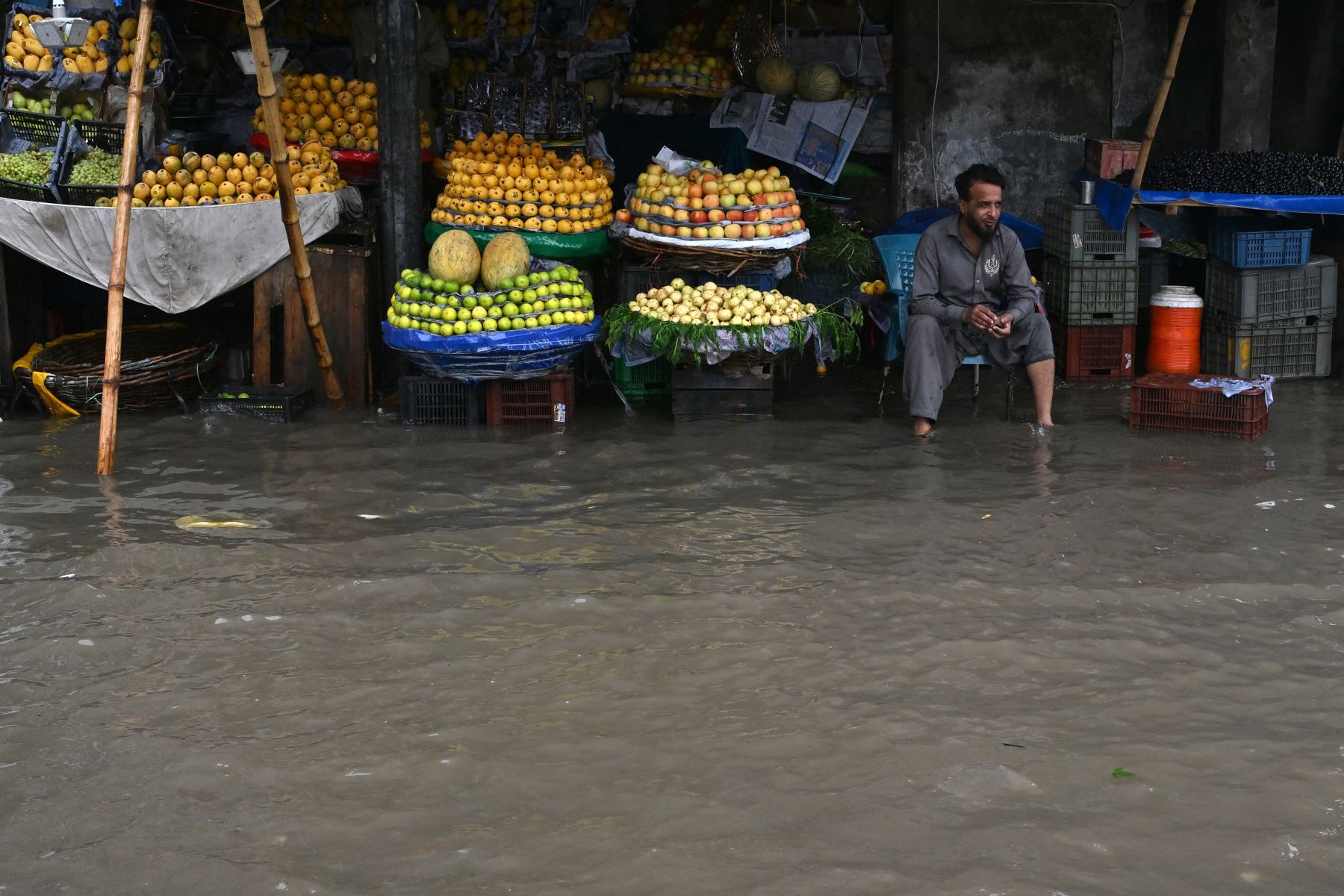 Un vendedor de fruta se encuentra sentado en su puesto de venta en una calle inundada tras las fuertes lluvias en Lahore, Pakistán, el 25 de julio de 2026. Foto: AFP