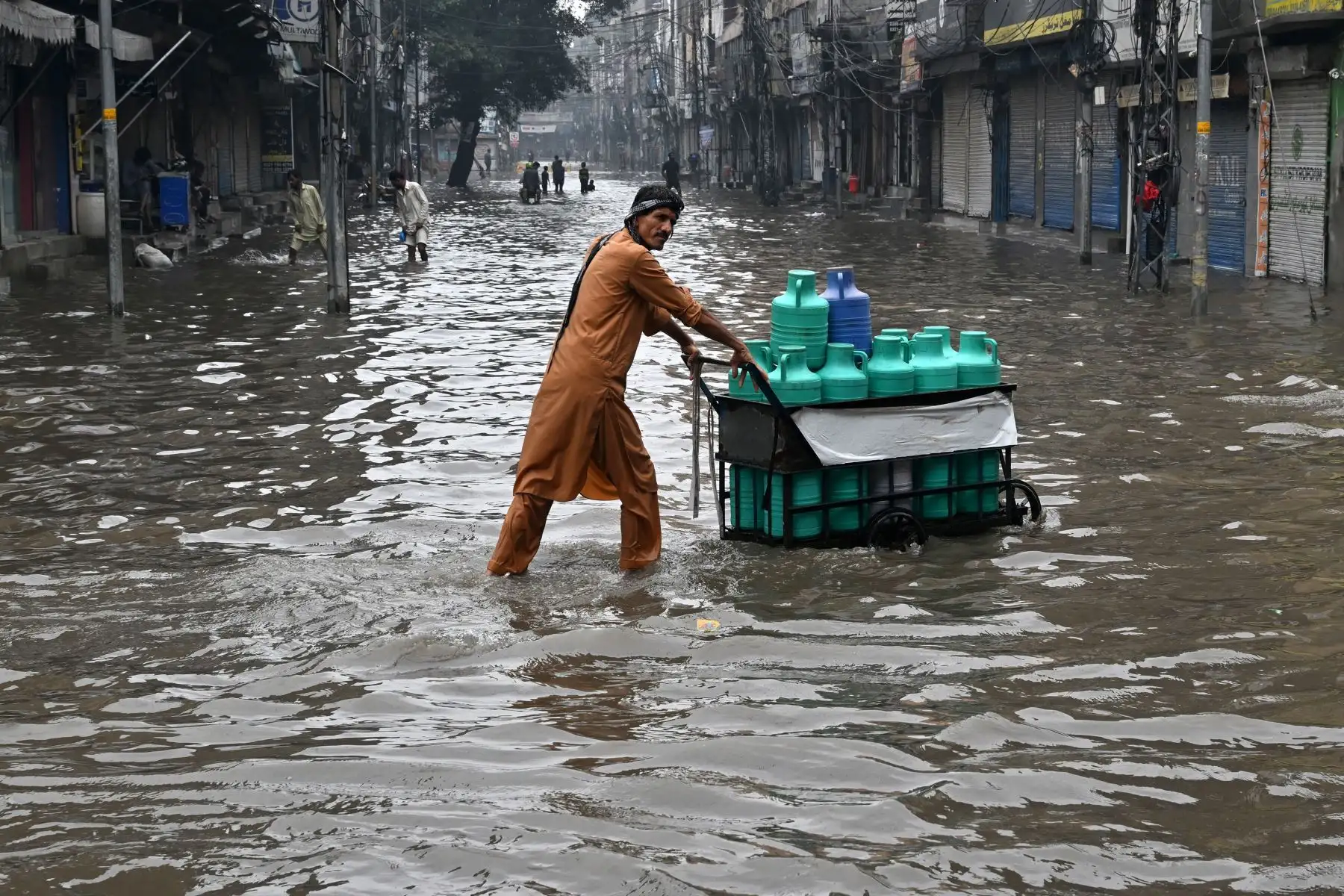 Un hombre empuja un carro cargado de bidones de agua por una calle inundada tras las fuertes lluvias en Lahore, Pakistán, el 25 de julio de 2026. Foto: AFP