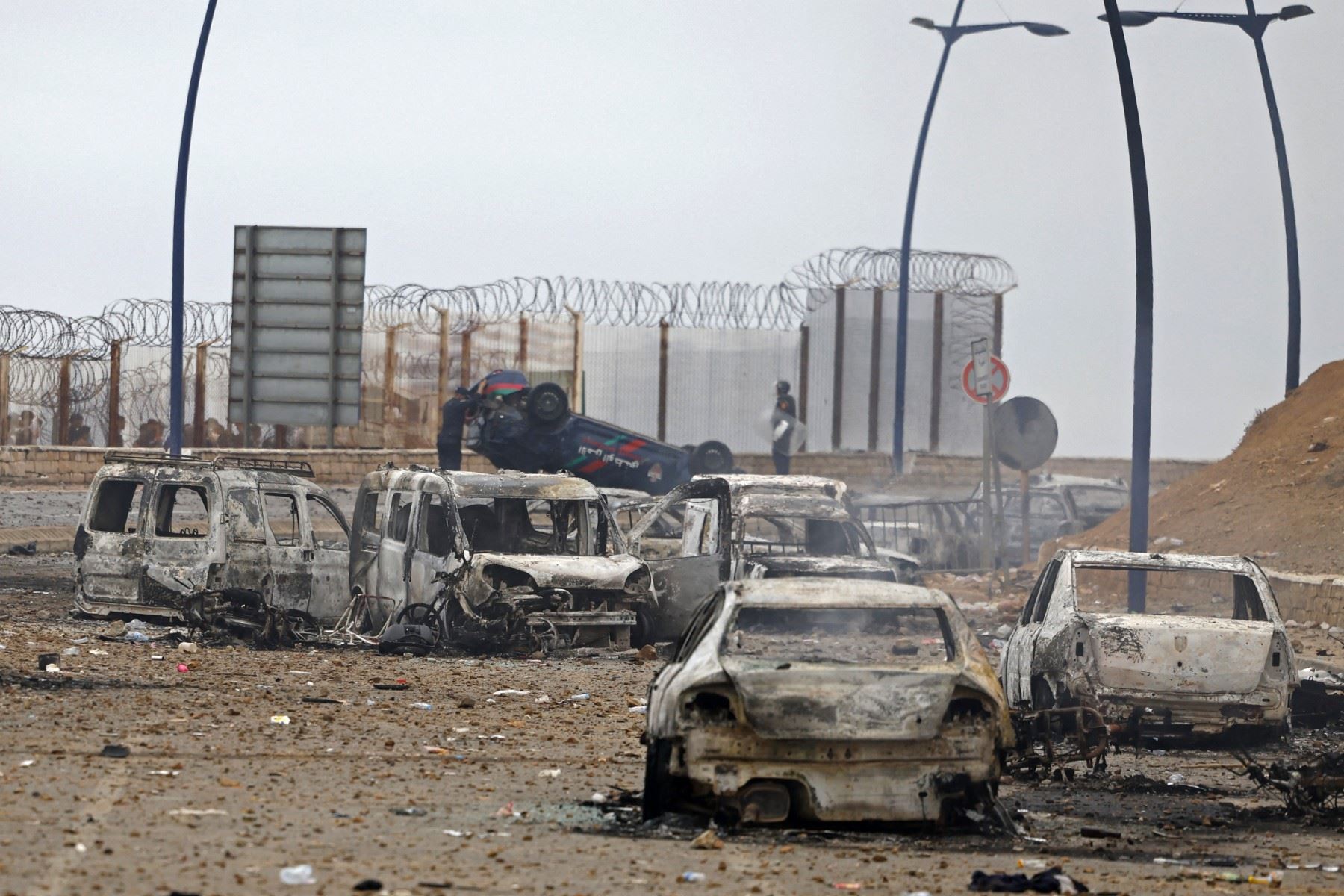 Miembros de las fuerzas de seguridad marroquíes se congregan junto a un vehículos volcados y dañados en el lugar de los enfrentamientos cerca de Fnideq, en la frontera entre Marruecos y España. Foto: AFP