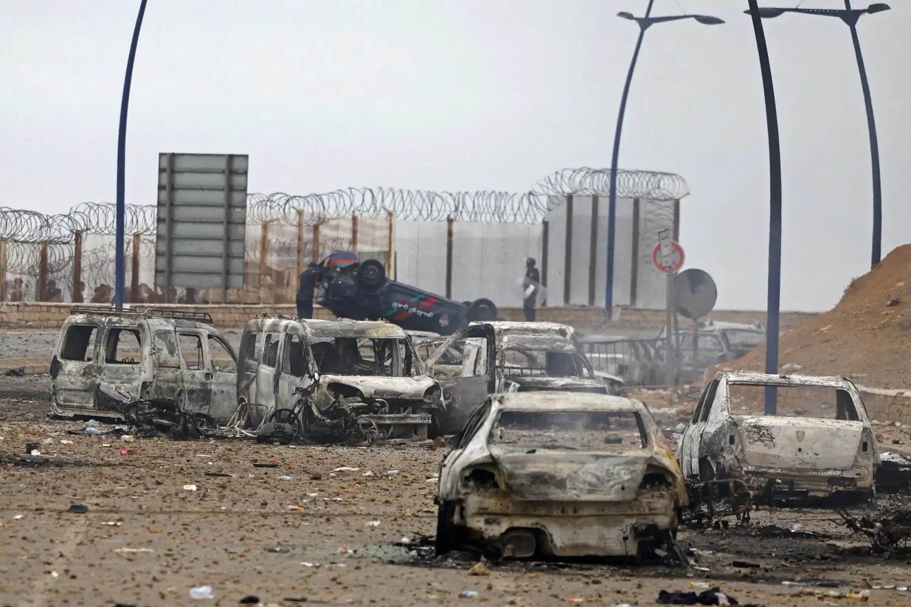 Miembros de las fuerzas de seguridad marroquíes se congregan junto a un vehículos volcados y dañados en el lugar de los enfrentamientos cerca de Fnideq, en la frontera entre Marruecos y España. Foto: AFP
