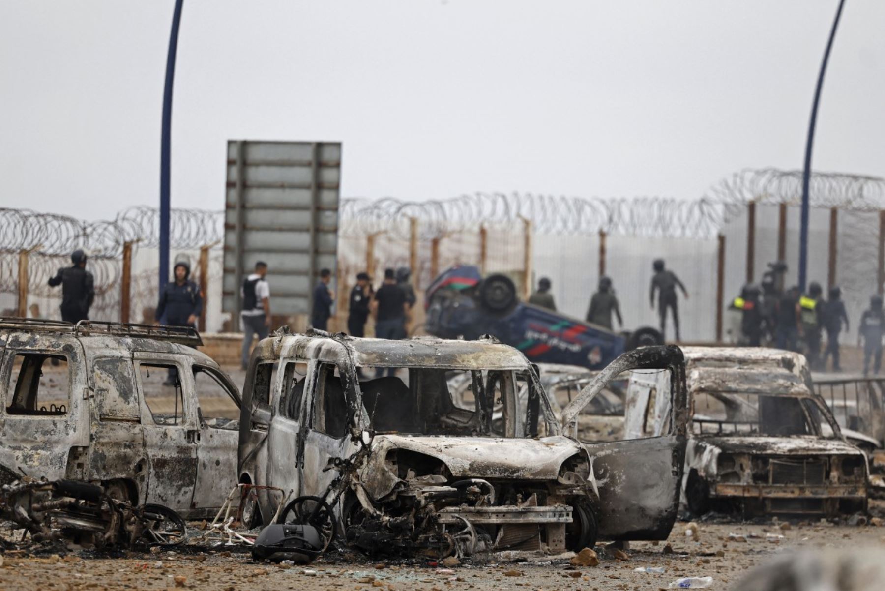Miembros de las fuerzas de seguridad marroquíes se congregan junto a un vehículos volcados y dañados en el lugar de los enfrentamientos cerca de Fnideq, en la frontera entre Marruecos y España. Foto: AFP