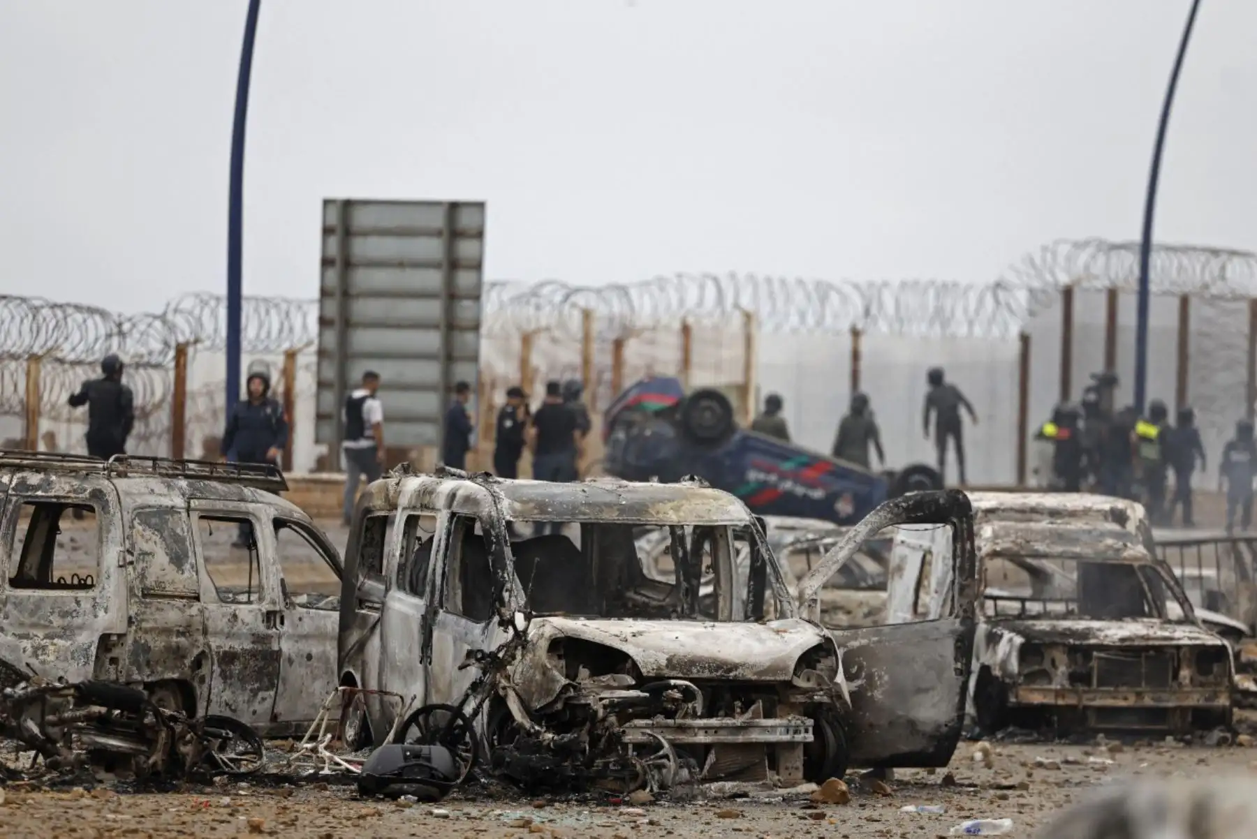 Miembros de las fuerzas de seguridad marroquíes se congregan junto a un vehículos volcados y dañados en el lugar de los enfrentamientos cerca de Fnideq, en la frontera entre Marruecos y España. Foto: AFP