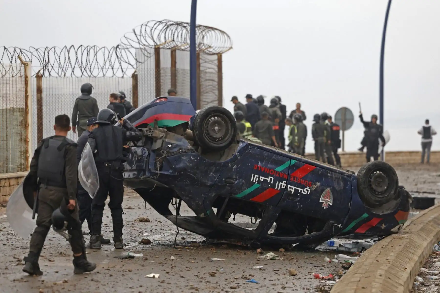Miembros de las fuerzas de seguridad marroquíes se congregan junto a un vehículos volcados y dañados en el lugar de los enfrentamientos cerca de Fnideq, en la frontera entre Marruecos y España. Foto: AFP