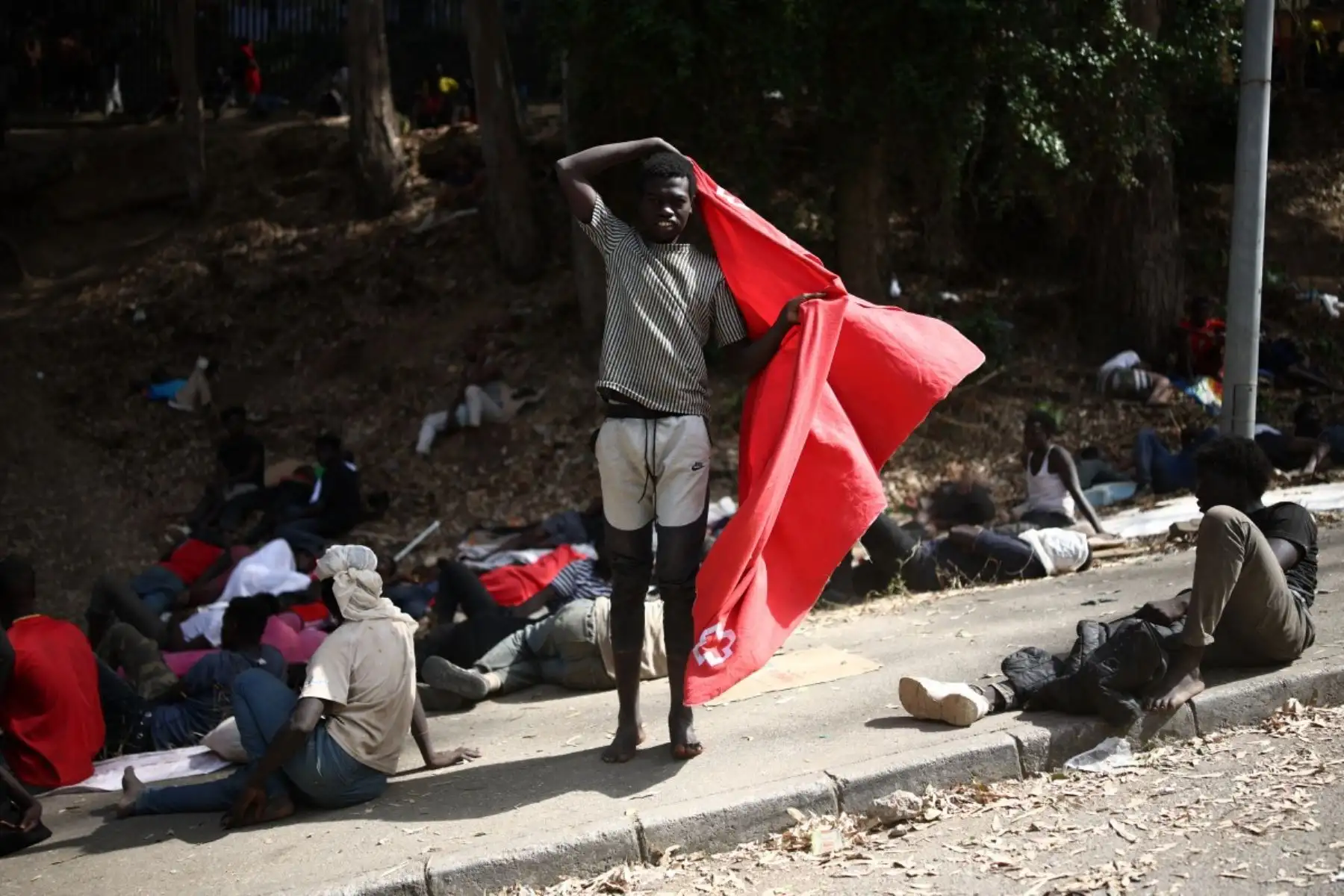 Un migrante lleva una manta roja mientras otros descansan a las afueras del centro de acogida temporal CETI en el enclave español de Ceuta, en el norte de África, el 1 de agosto de 2026. Foto: AFP
