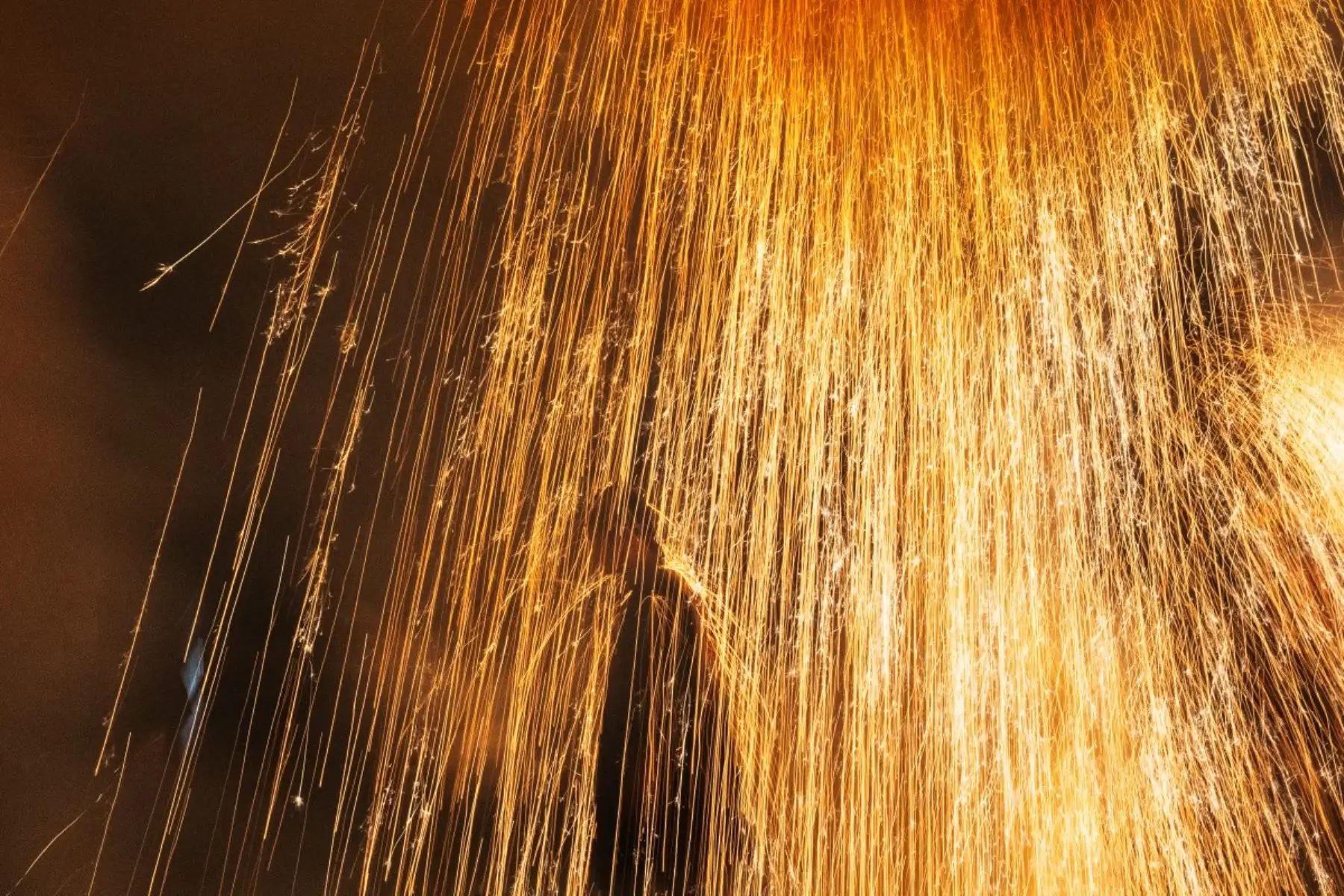 Un tezutsu-shu, un artista tradicional de fuegos artificiales sostenidos con el brazo, es rociado con chispas de tezutsu hanabi, tubos de bambú hechos a mano rellenos de pólvora que estallan en una imponente columna de chispas y llamas, durante el Festival de Fuegos Artificiales Sostenidos con el Brazo de Tatebayashi en Tatebayashi, Prefectura de Gunma, el 25 de julio de 2026. Foto: AFP