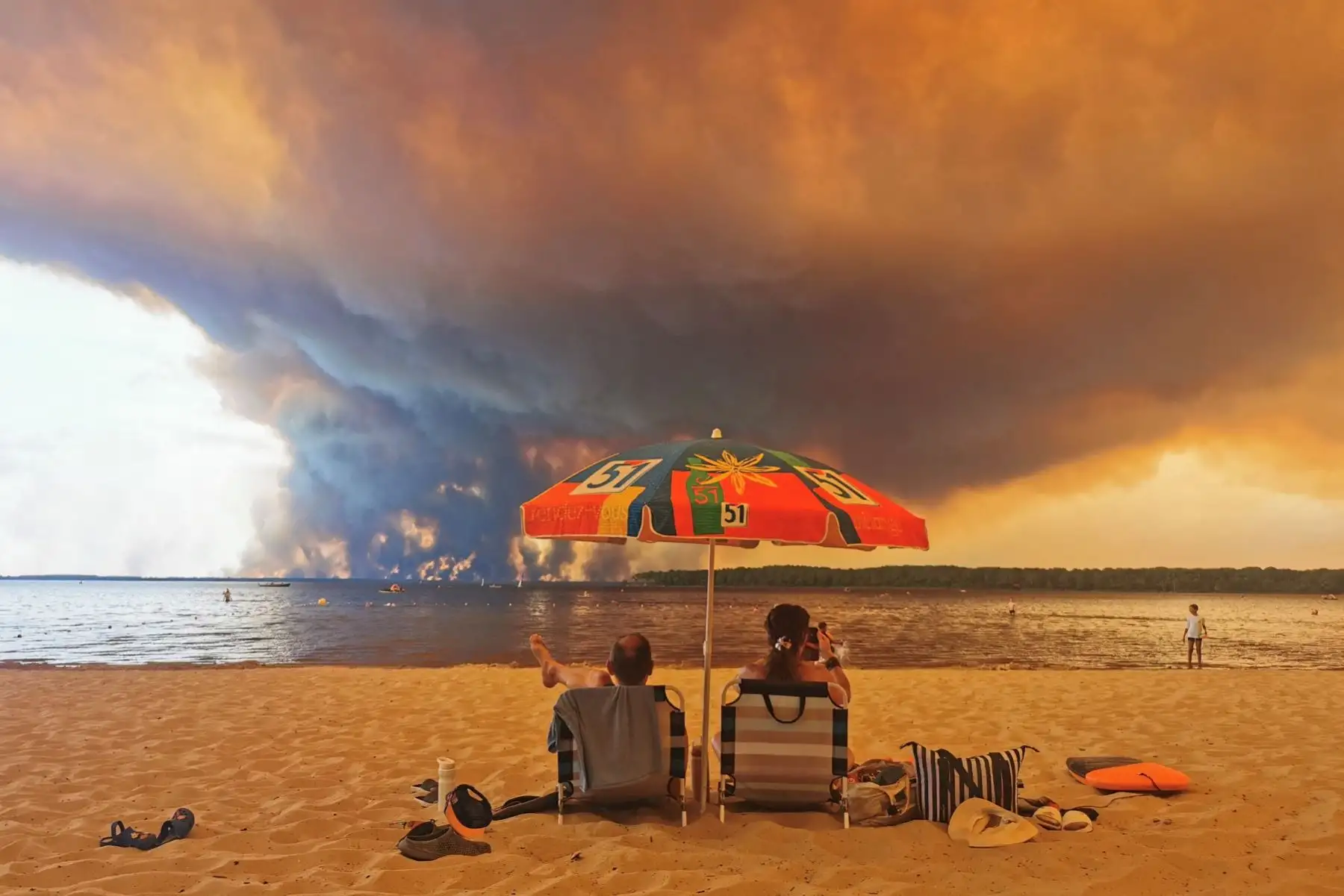 Los bañistas descansan en la playa de Moutchic, a orillas del lago Lacanau (Etang de Lacanau), en Lacanau, al suroeste de Francia, mientras columnas de humo se elevan hacia el cielo procedentes del incendio forestal de la Gironda. Foto: AFP