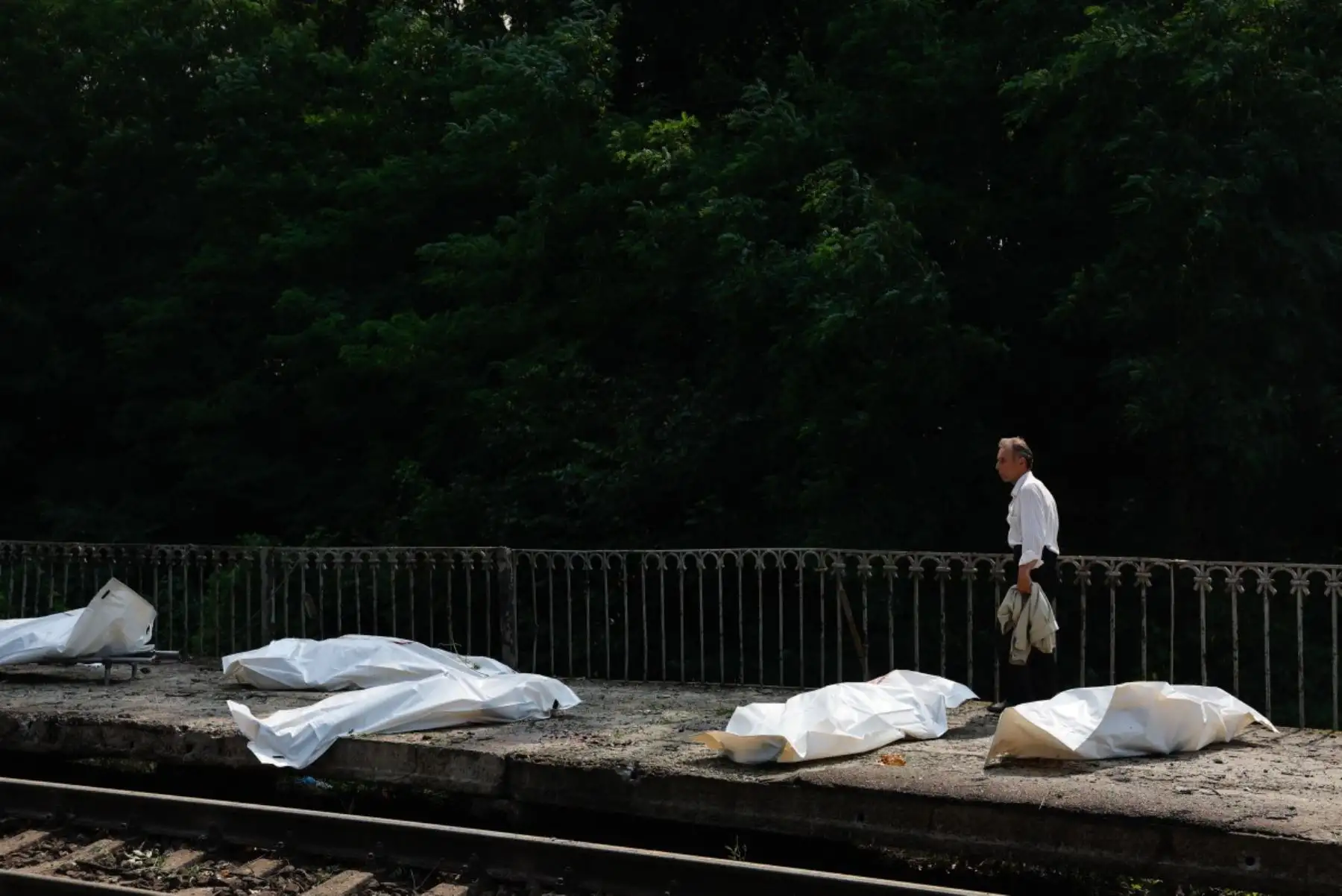 Un hombre pasa junto a los cuerpos en bolsas de plástico de personas que murieron durante un ataque con misiles balísticos y drones rusos en una estación de tren en la región de Kiev el 5 de agosto de 2026, en medio de la invasión rusa de Ucrania. Foto: AFP