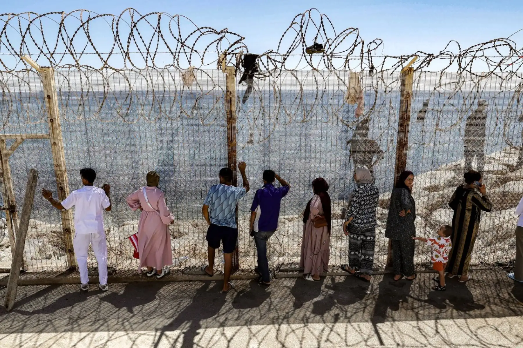 Familiares y amigos esperan junto a una valla coronada con alambre de espino el regreso de personas que habían cruzado previamente al enclave español de Ceuta, en el paso fronterizo marroquí de Bab Sebta, en las afueras de Fnideq, el 2 de agosto de 2026. Foto: AFP