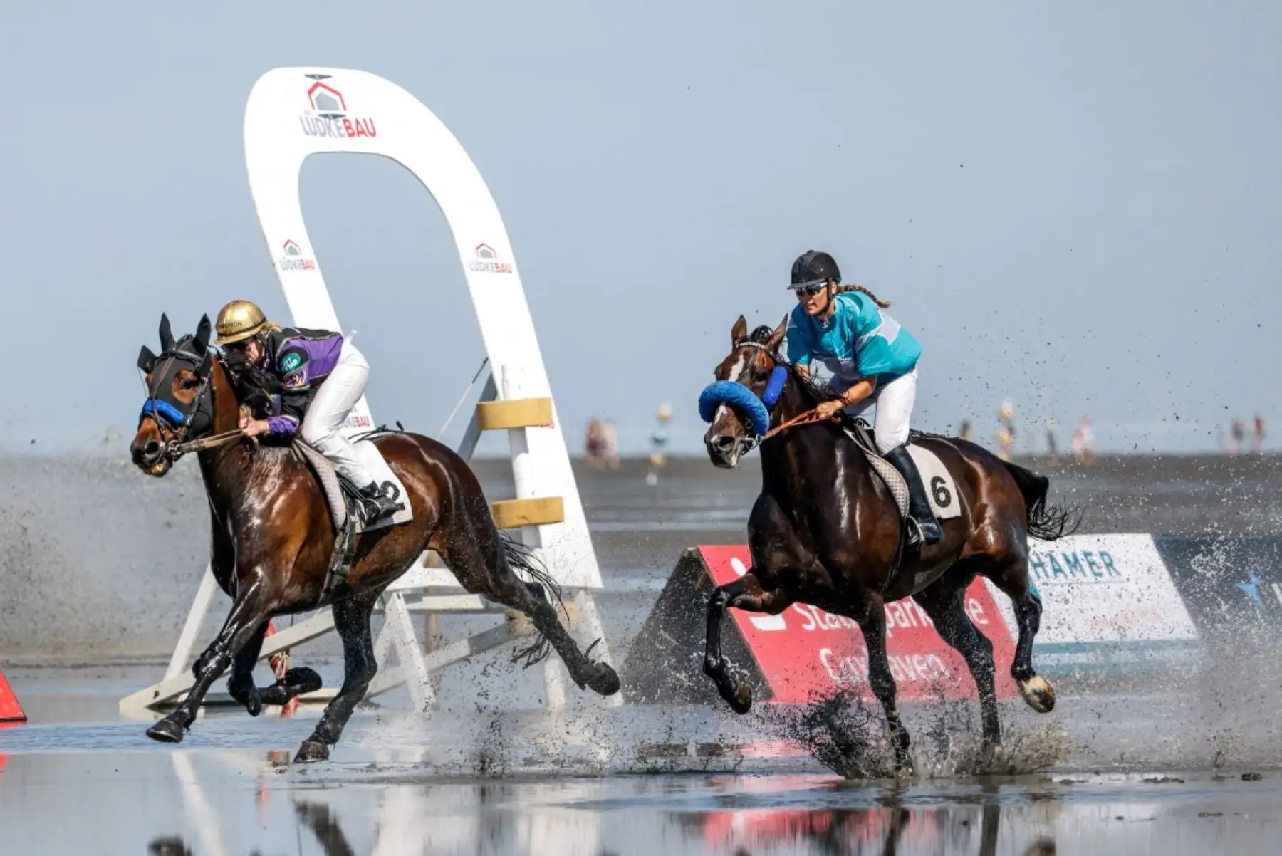 Las jinetes de trote Ronja Walter (izquierda), con Fox Double Trouble, y Nicole Holzschuh, con IT Security, compiten durante la 90.ª edición de la carrera de caballos Duhner Wattrennen, que se celebra en las marismas del estuario del Elba durante la bajamar en Cuxhaven-Duhnen, Alemania, el 9 de agosto de 2026. La 90.ª edición de la Duhner Wattrennen, que tiene lugar en el mar de Frisia, en las marismas del río Elba, es una carrera de caballos que se celebra en el lecho marino durante la bajamar. Foto: AFP