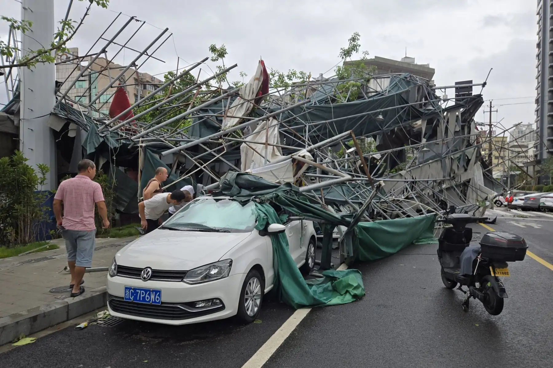 Unas personas observan un automóvil dañado por un andamio que cayó durante el paso del tifón Dolphin en Wenzhou, provincia de Zhejiang, China. Foto: EFE