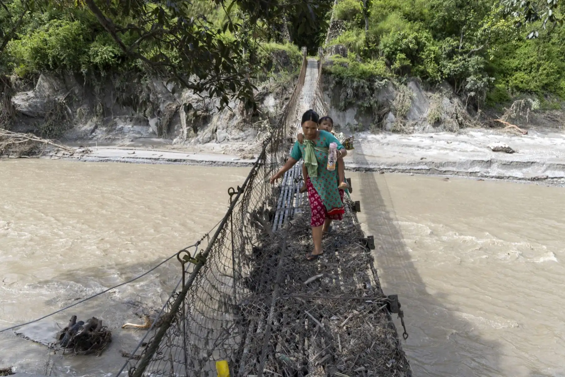 Personas cruzan un puente colgante dañado tras las inundaciones repentinas a lo largo de las orillas del río Trishuli en el distrito de Dhading, Nepal. Foto: EFE