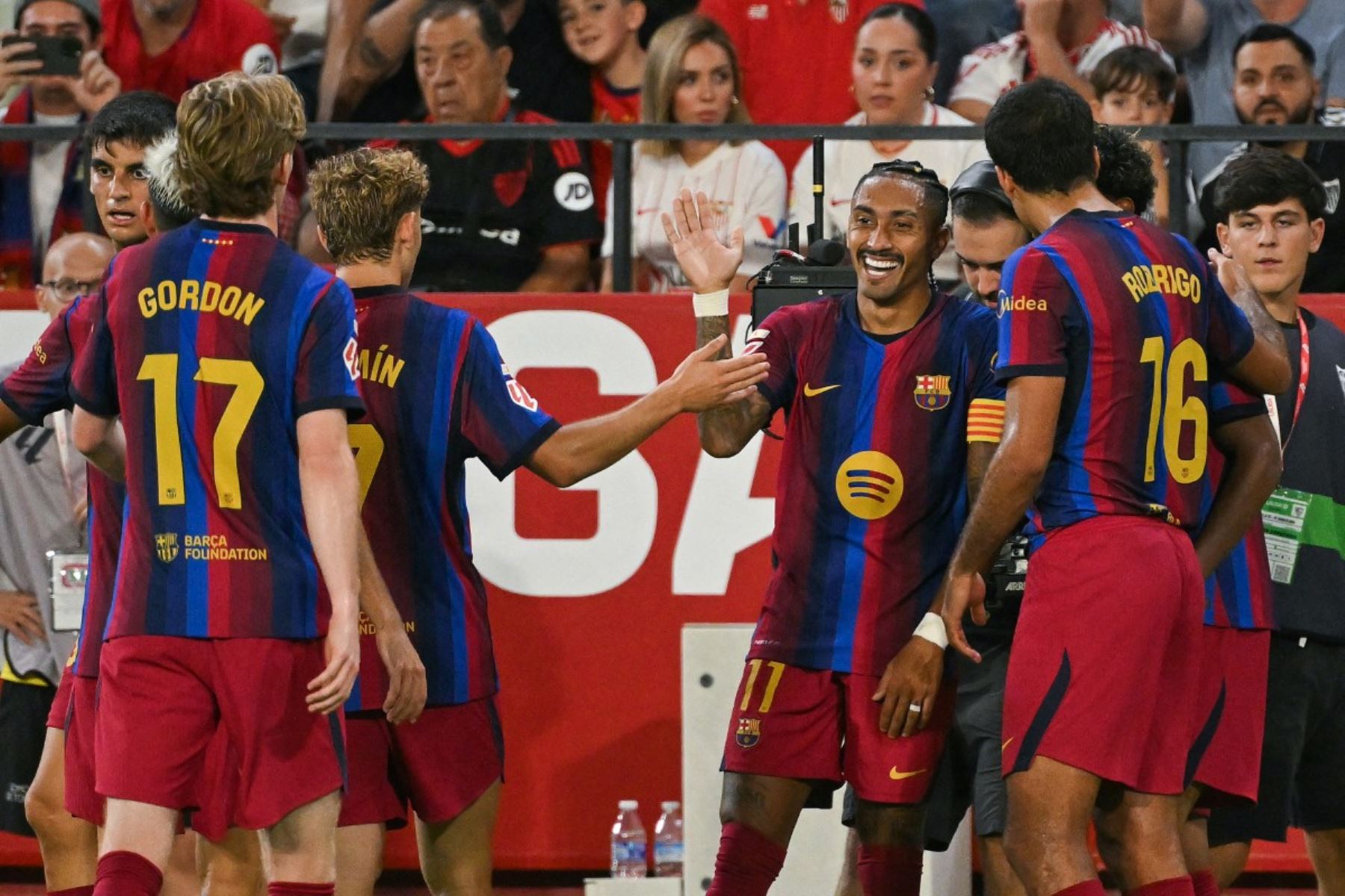 El delantero brasileño del Barcelona, ​​Raphinha (C), número 11, celebra con sus compañeros tras marcar el tercer gol de su equipo durante el partido de la liga española entre el Sevilla FC y el FC Barcelona en el estadio Ramón Sánchez Pizjuán de Sevilla, el 19 de septiembre de 2026. (Foto de JORGE GUERRERO / AFP)