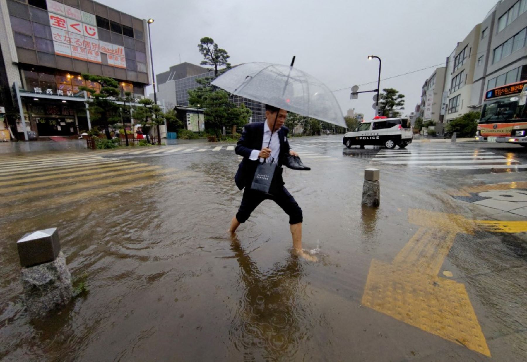 Un hombre con sus zapatos en la mano camina por una intersección inundada tras las fuertes lluvias provocadas por el tifón Dujuan en la ciudad de Kamakura, prefectura de Kanagawa, Japón, el 21 de septiembre de 2026. Foto: AFP