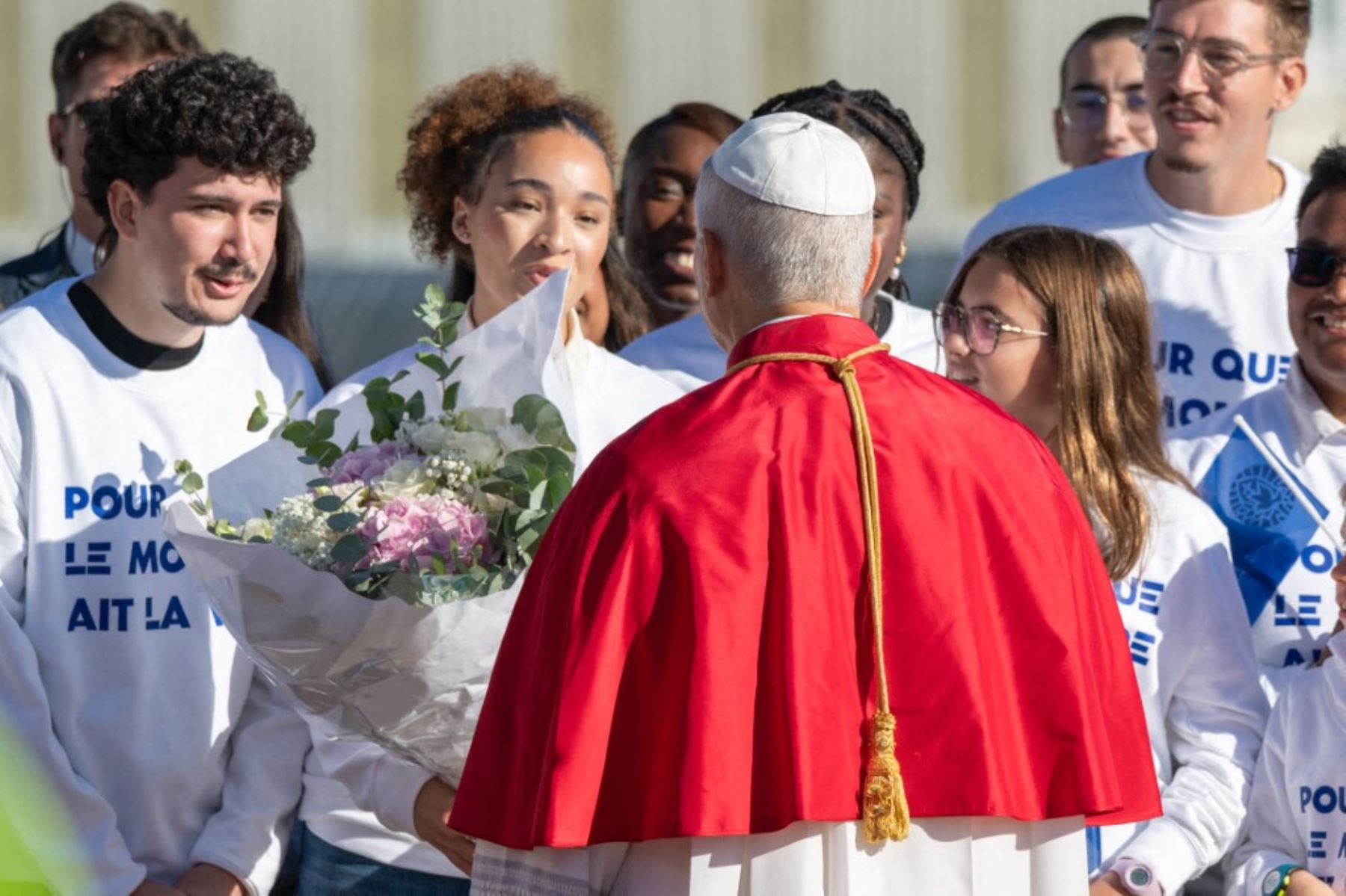 El papa León XIV, visto de espaldas, conversa con jóvenes que acudieron a recibirlo a su llegada al aeropuerto de Francia. Foto: AFP