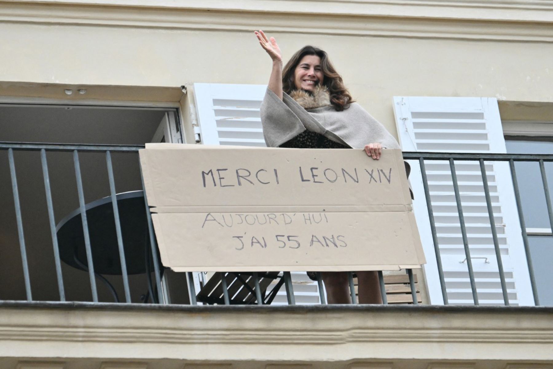 Una mujer saluda desde su balcón sosteniendo una pancarta que dice "Gracias, Papa León XIV; hoy cumplo 55 años", durante el segundo día de su visita a Francia. (Foto: ANDINA/ AFP