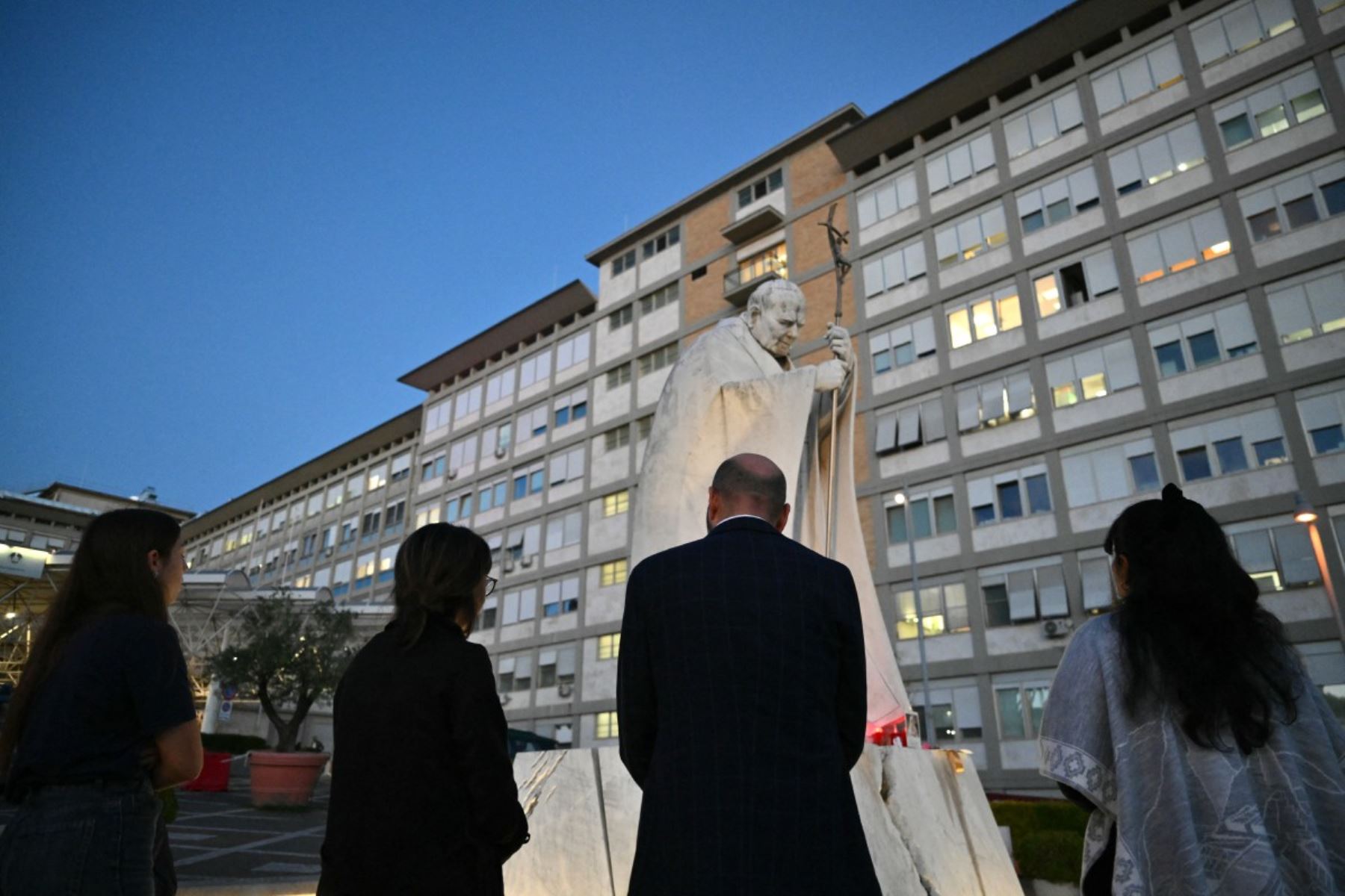 Los fieles rezan frente a la estatua de Juan Pablo II a las afueras del Hospital Universitario Gemelli, donde el Papa León XIV se recupera tras someterse a una cirugía para extirpar un tumor canceroso de su pulmón derecho, en Roma. Foto: AFP