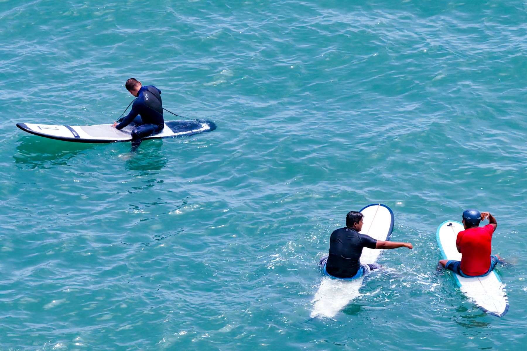 Tres surfistas aguardan el momento indicado sobre sus tablas en medio de las tranquilas aguas turquesas. Foto: ANDINA/Ricardo Cuba