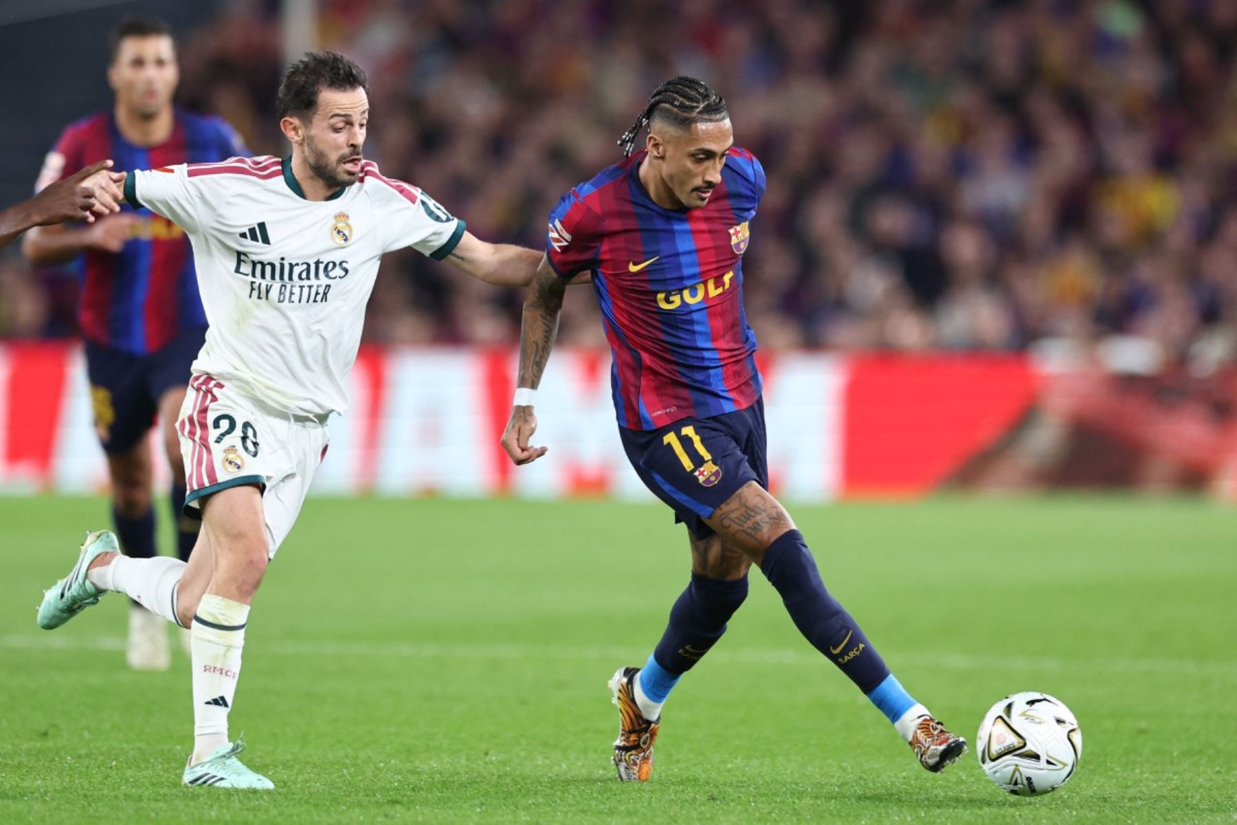 El delantero brasileño del Barcelona, ​​Raphinha, golpea el balón mientras es presionado por el centrocampista portugués del Real Madrid, Bernardo Silva  durante el partido de la liga española de fútbol entre el FC Barcelona y el Real Madrid CF en el estadio Camp Nou, en Barcelona. Foto: AFP