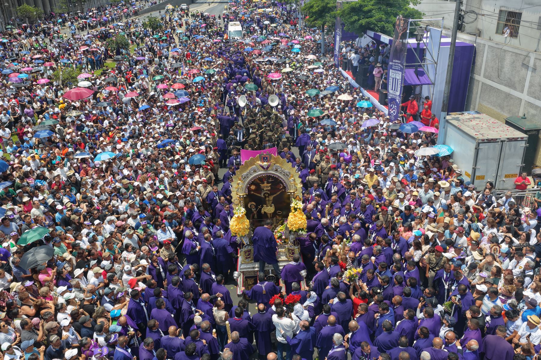 Vista aérea de las andas del Señor de los Milagros rodeadas por una multitud de fieles vestidos de morado. Durante el homenaje organizado por Editora Perú, los colaboradores de la institución entregaron flores y cirios como parte de las ofrendas a la sagrada imagen. Foto: ANDINA/Daniel Bracamonte.